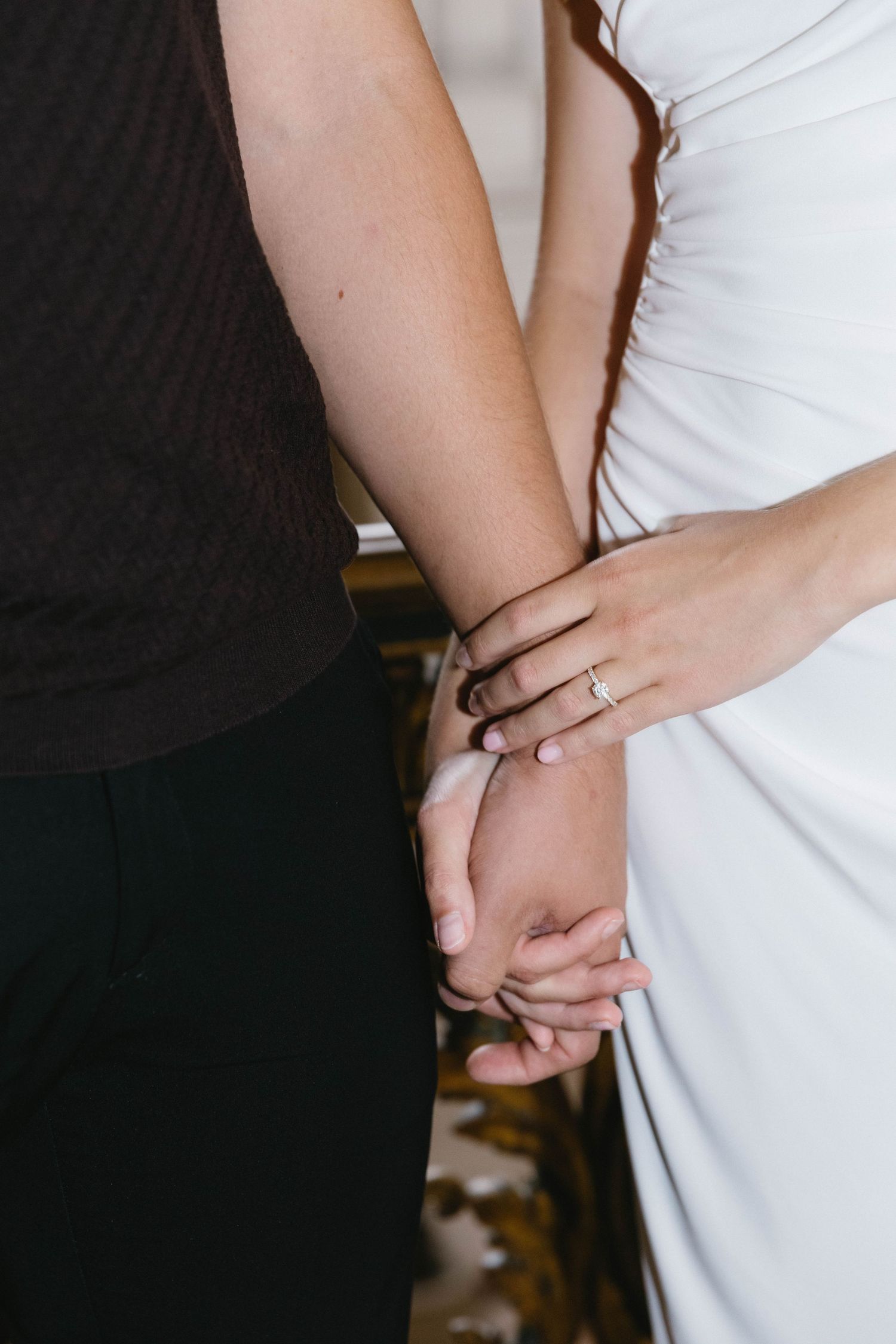 Close-up of hands embracing, showing a ring detail against white fabric.