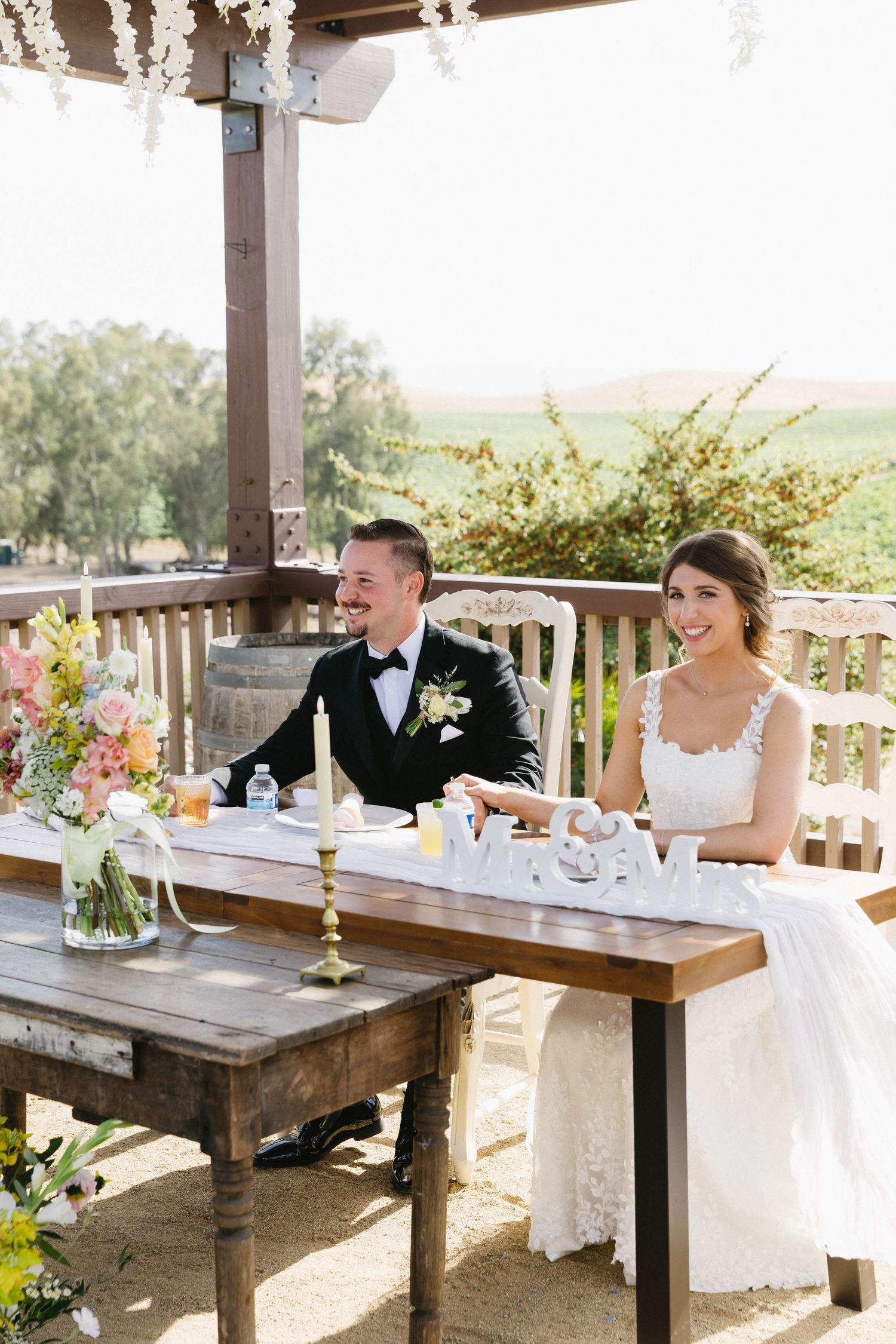 A joyful reception moment at a rustic outdoor table decorated with flowers.