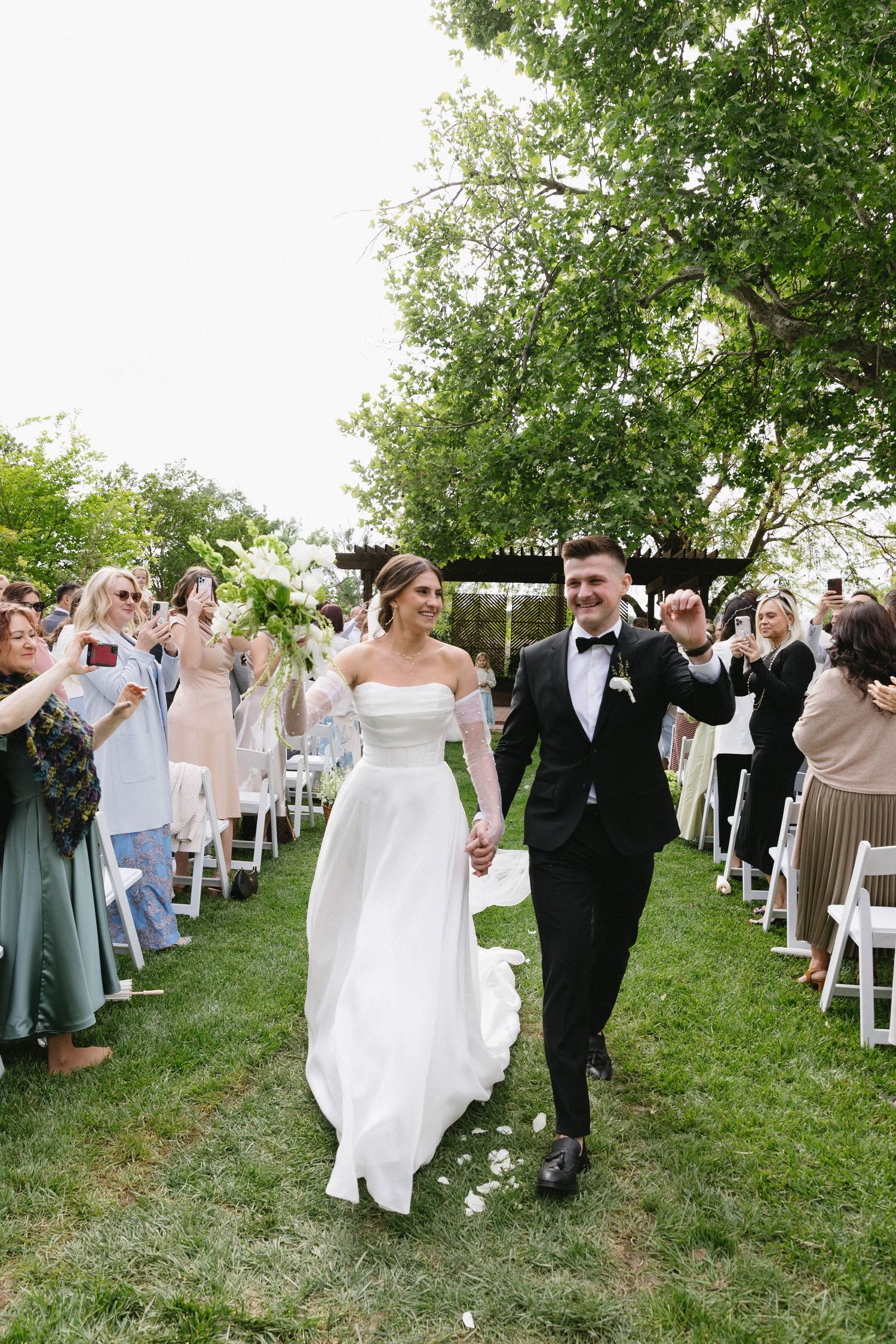 Wedding party dancing in a line across a grassy outdoor venue with white chairs.