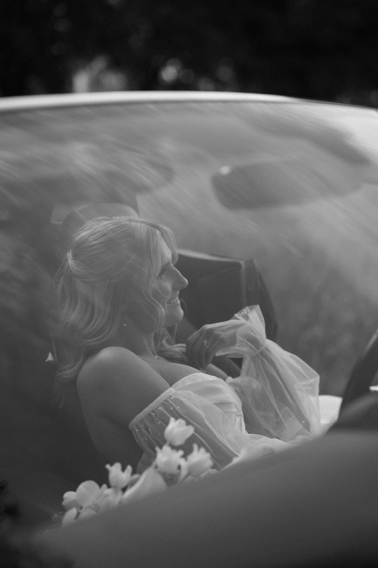 Artistic black and white photo through car window showing wedding couple's tender moment.