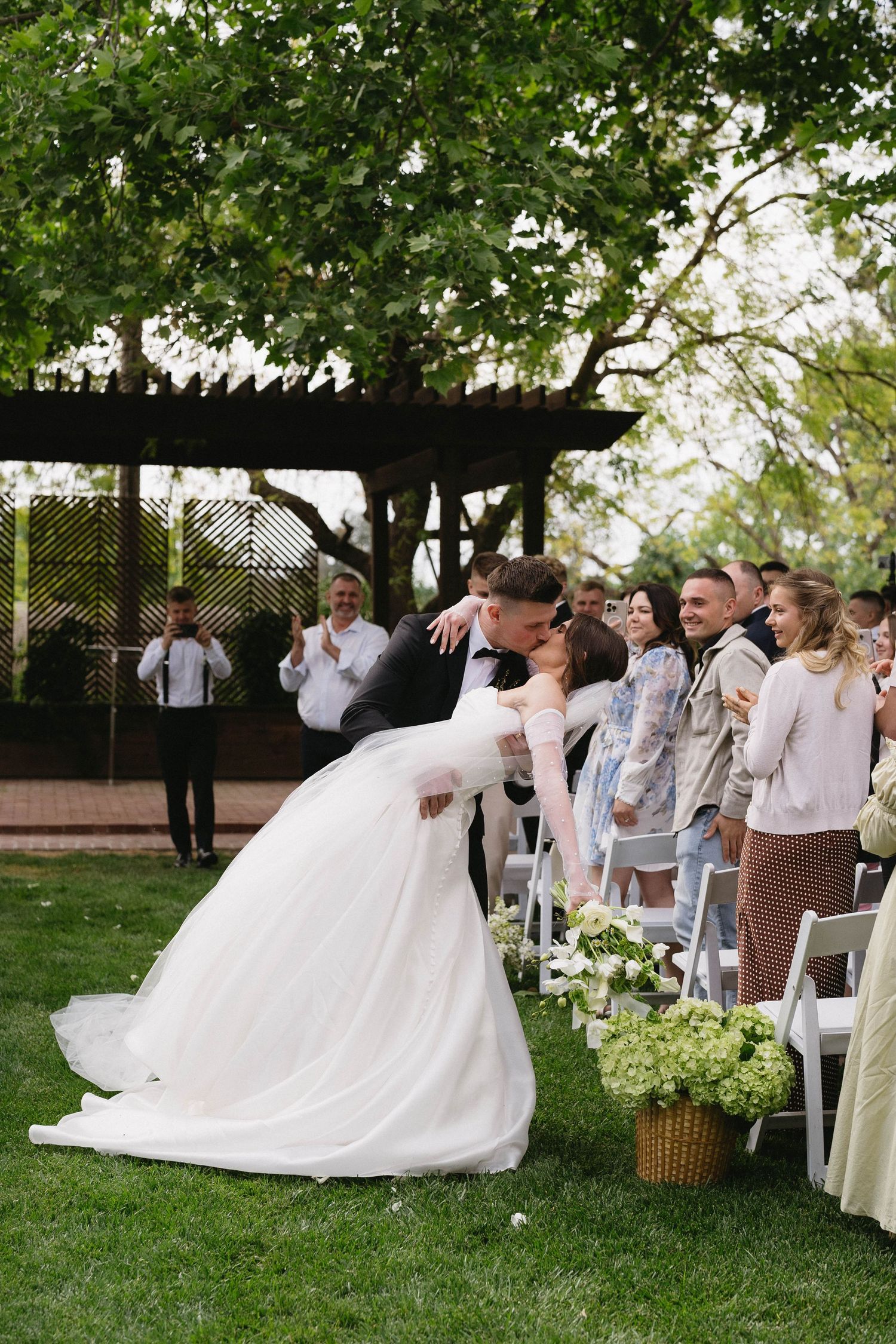 Outdoor wedding reception with dancing couples and white chairs on a manicured lawn.