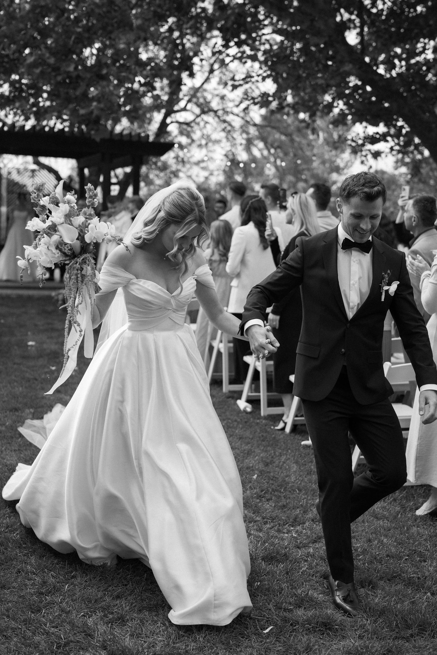 Black and white photo of wedding guests dancing in celebration on a lawn.