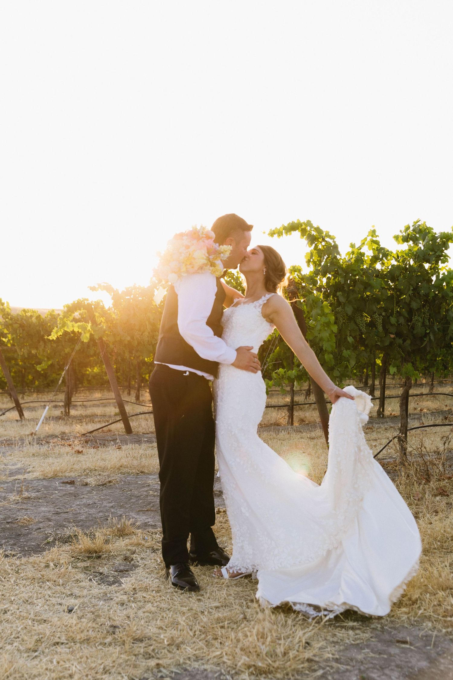 Newlyweds embrace in a sun-drenched vineyard during golden hour.