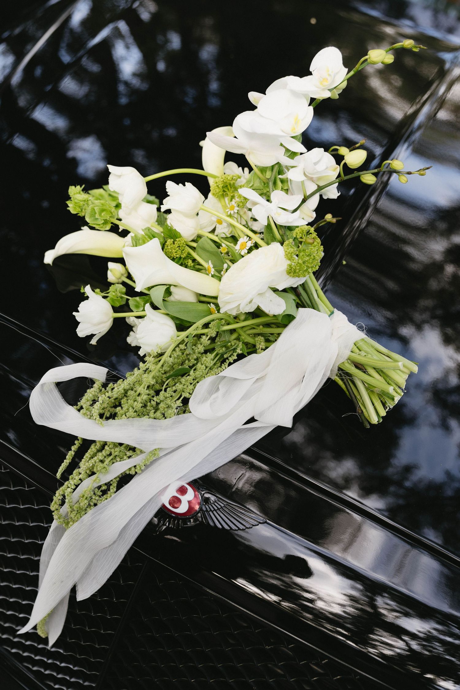 An elegant white floral bouquet with green accents tied with a satin ribbon rests on a shiny black surface.
