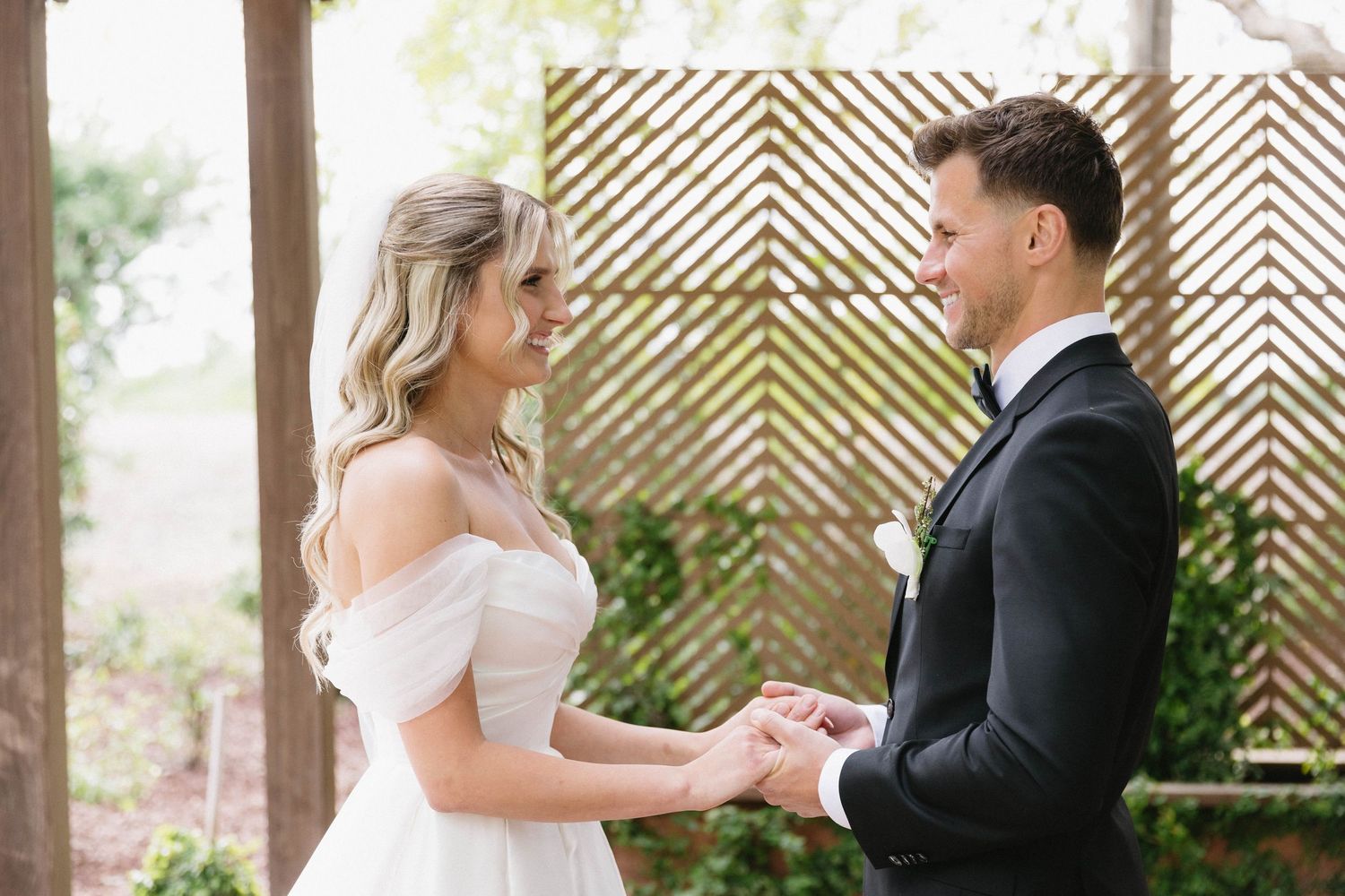 A couple shares a tender moment during their first look at an outdoor wedding venue with wooden lattice panels.