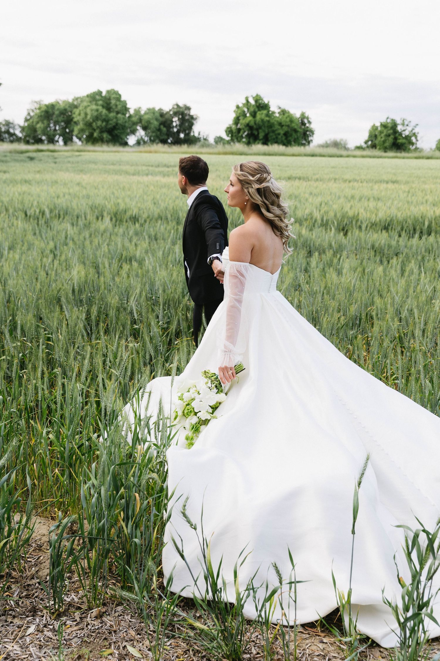 Wedding couple walking through a lush green wheat field with flowing white dress.