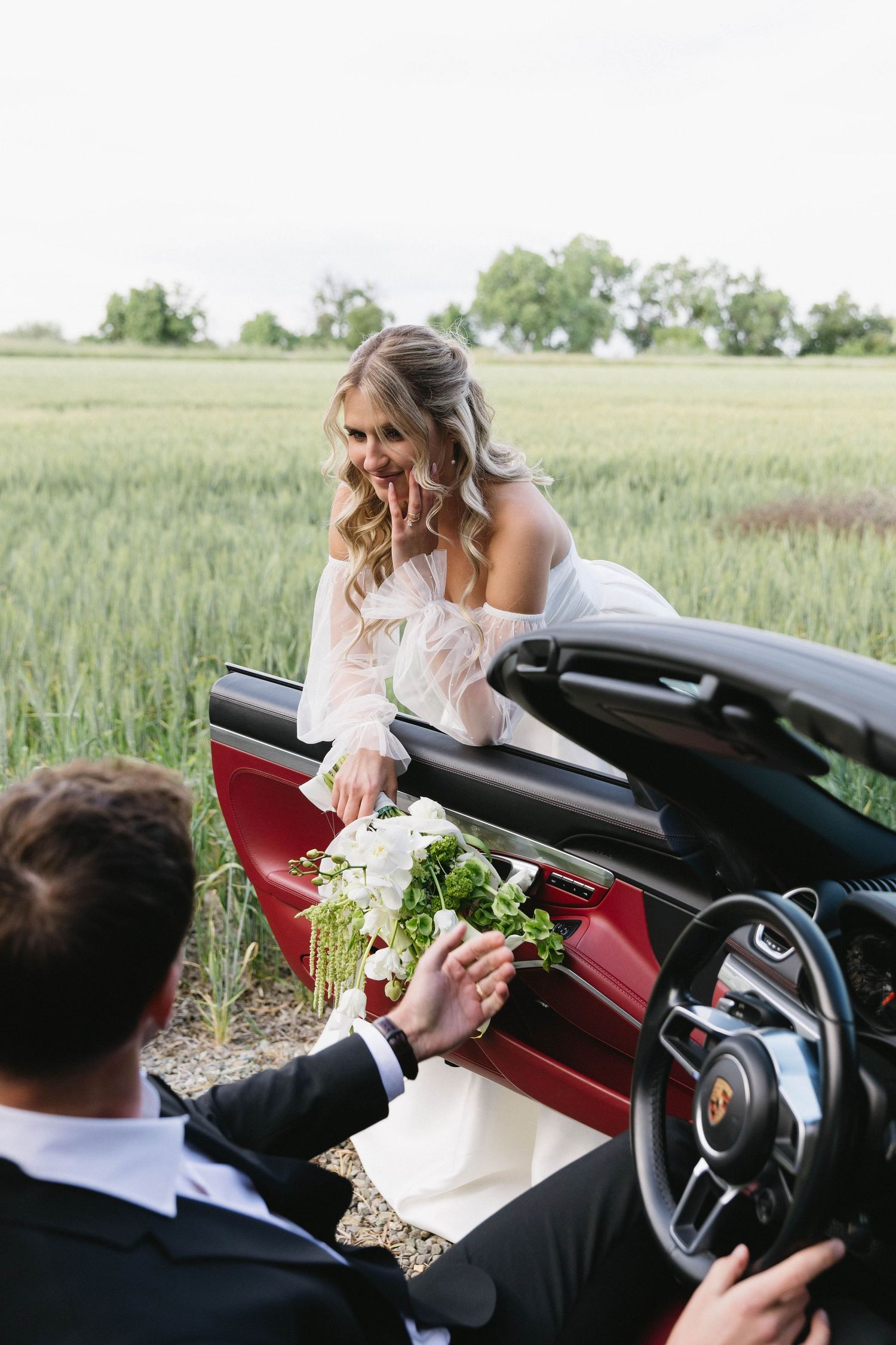 Newlyweds sharing a moment in a convertible Porsche with white bouquet.