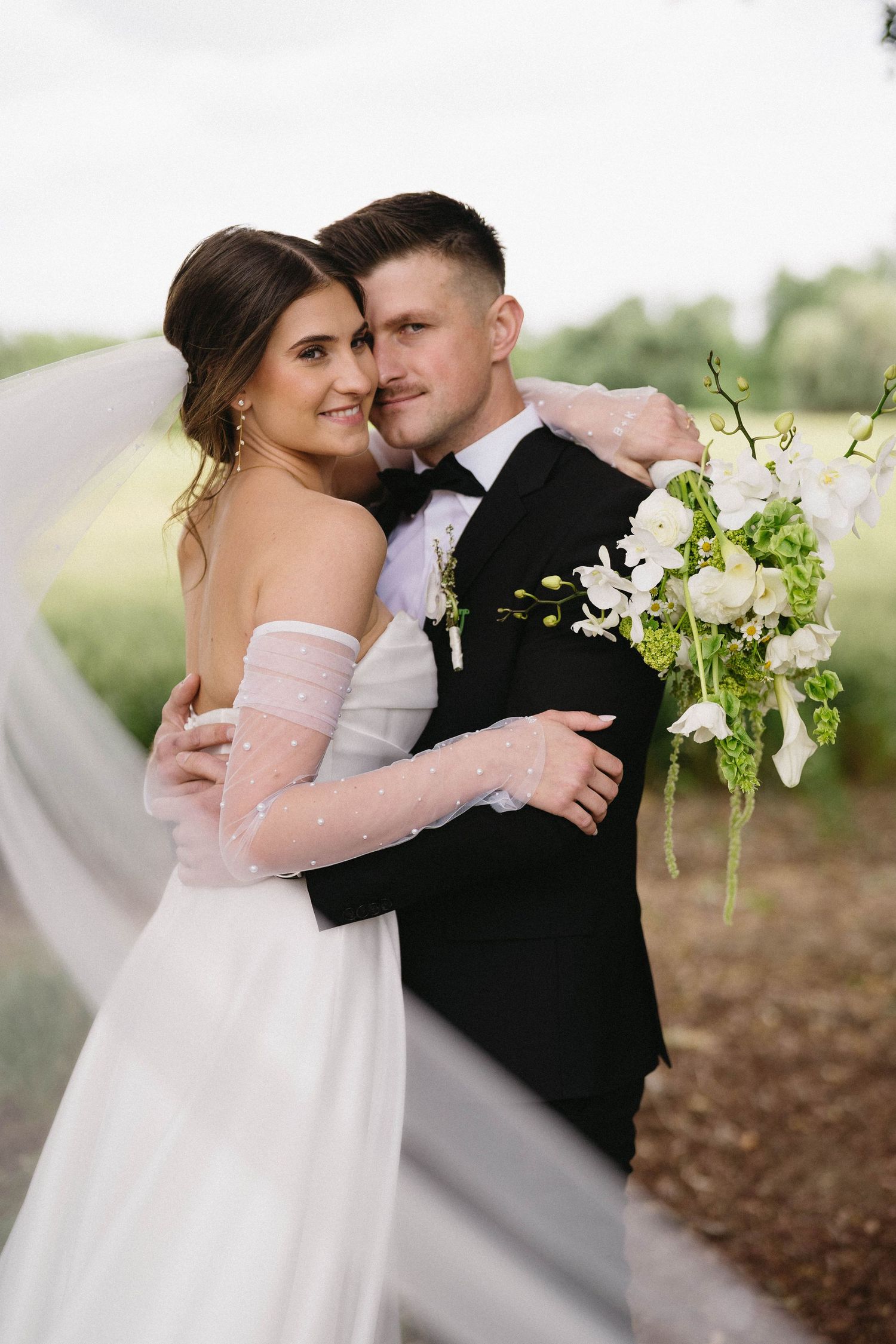 A romantic wedding portrait showing the couple embracing with white floral bouquet details.