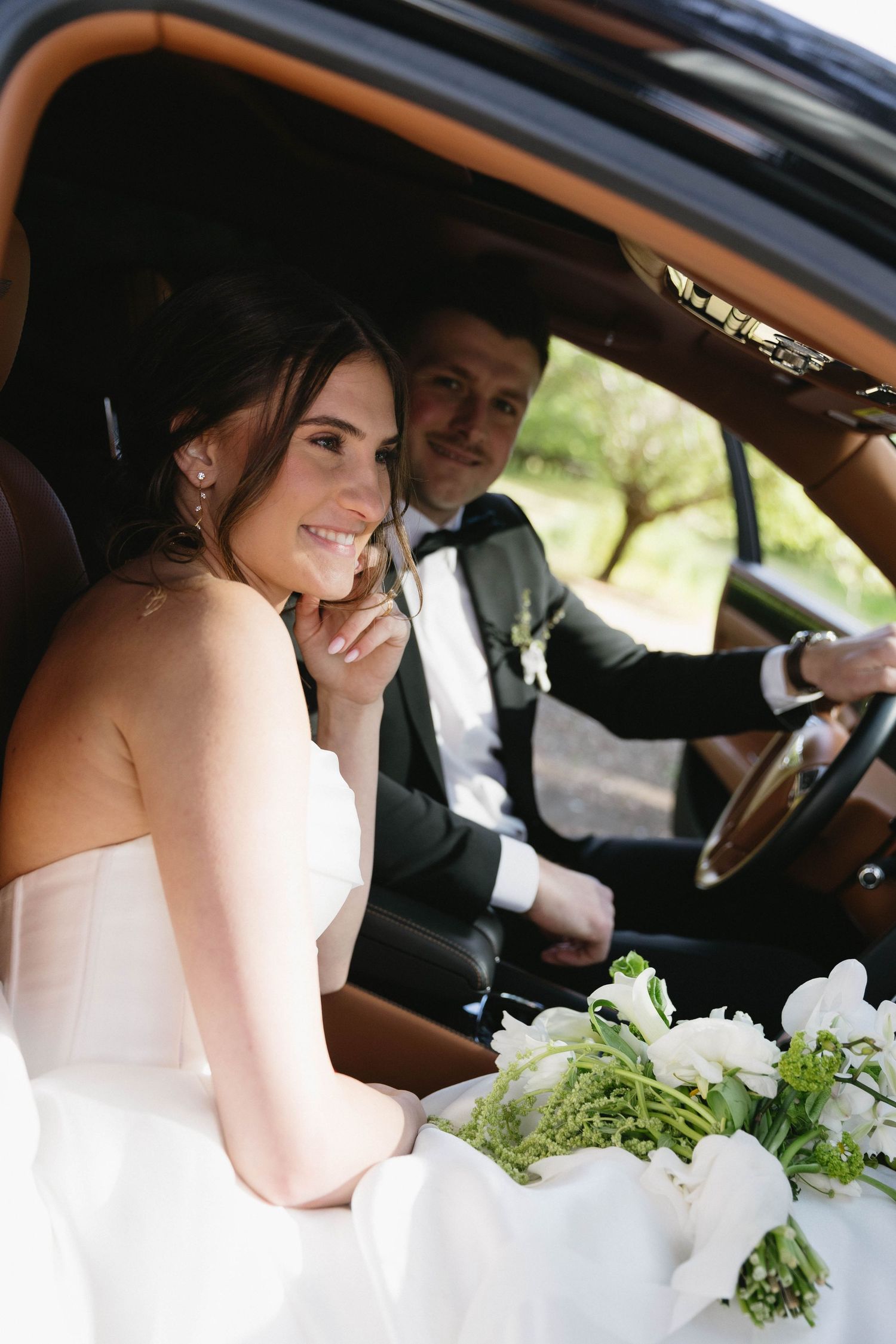 Wedding couple shares sweet moments inside luxury car with white floral bouquet.