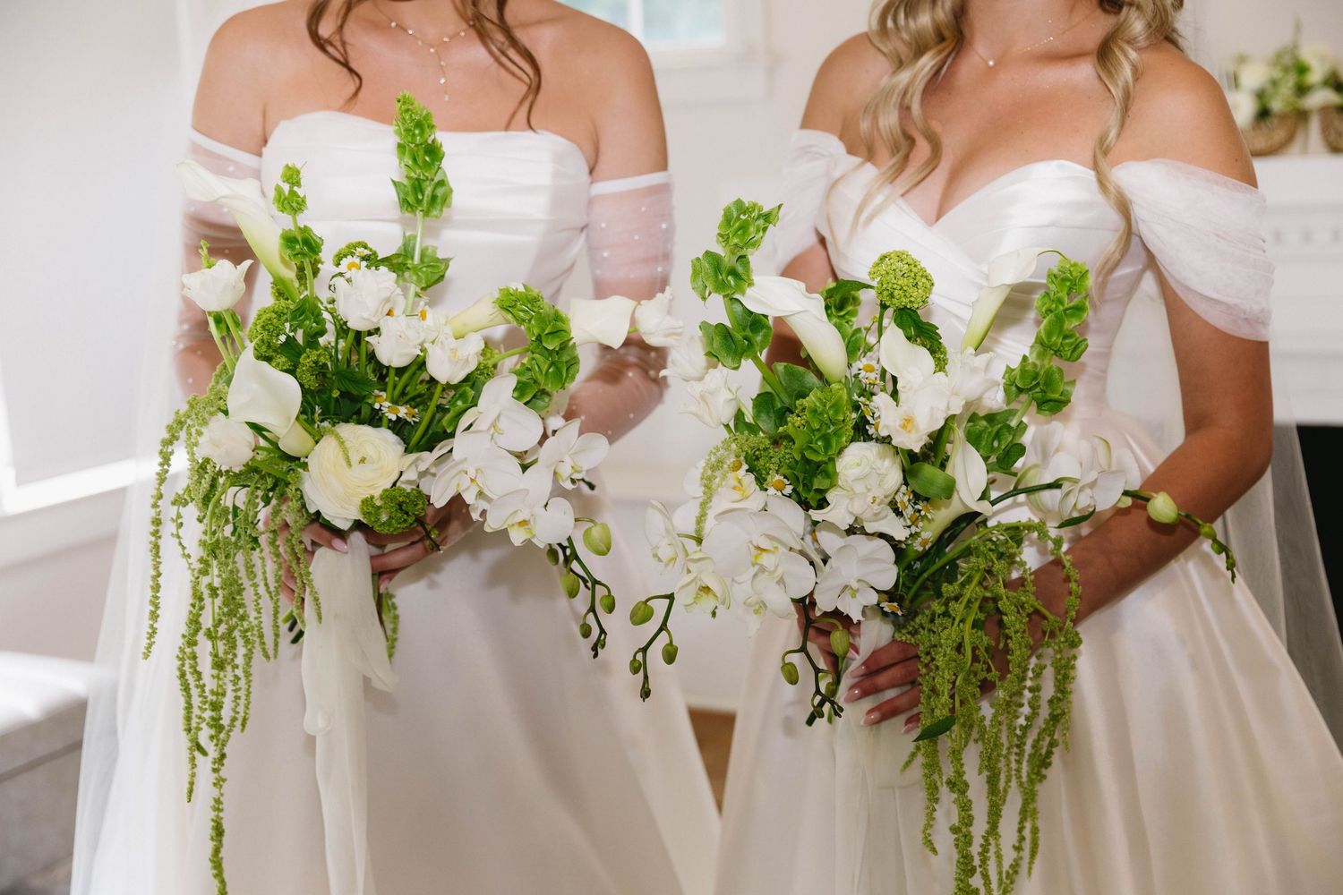 Row of bridesmaids in white dresses holding lush green and white floral bouquets.