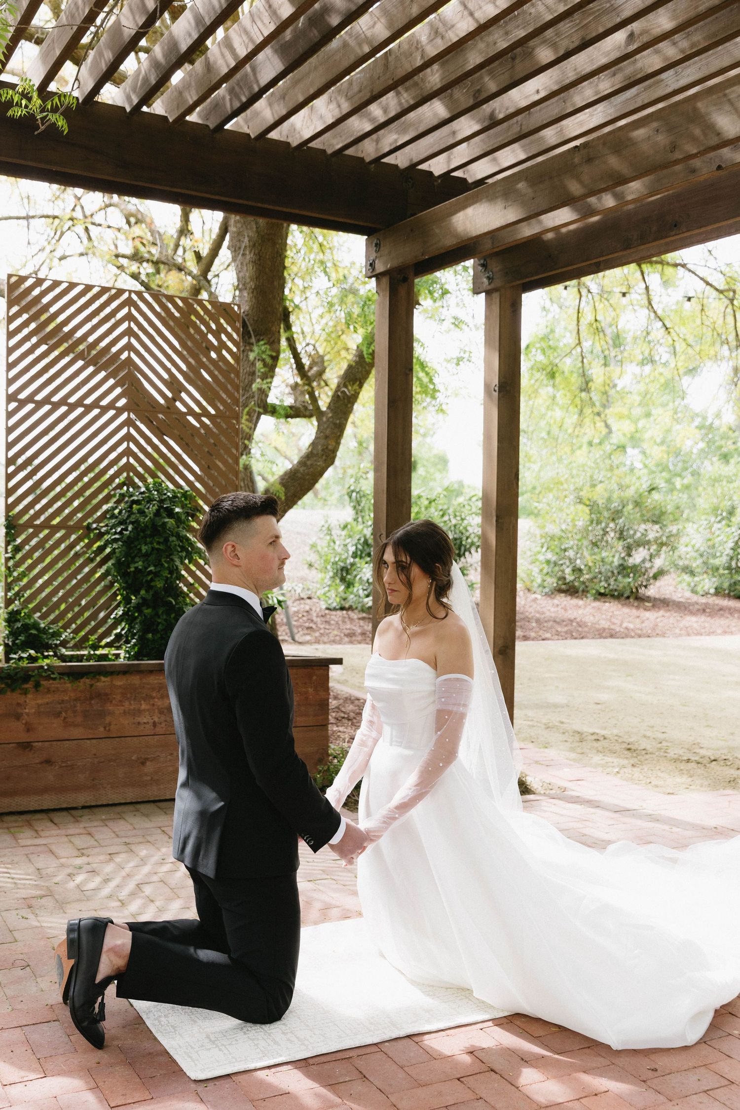 Wedding couple sharing private moments under a rustic wooden pergola with brick flooring.