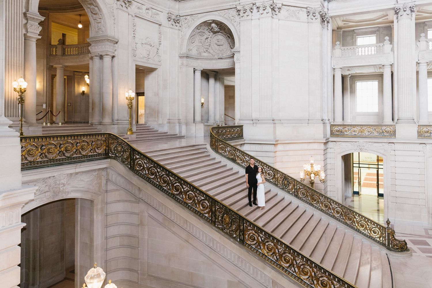 Elegant marble staircase with ornate gold railings inside a grand historic government building with white columns and walls.
