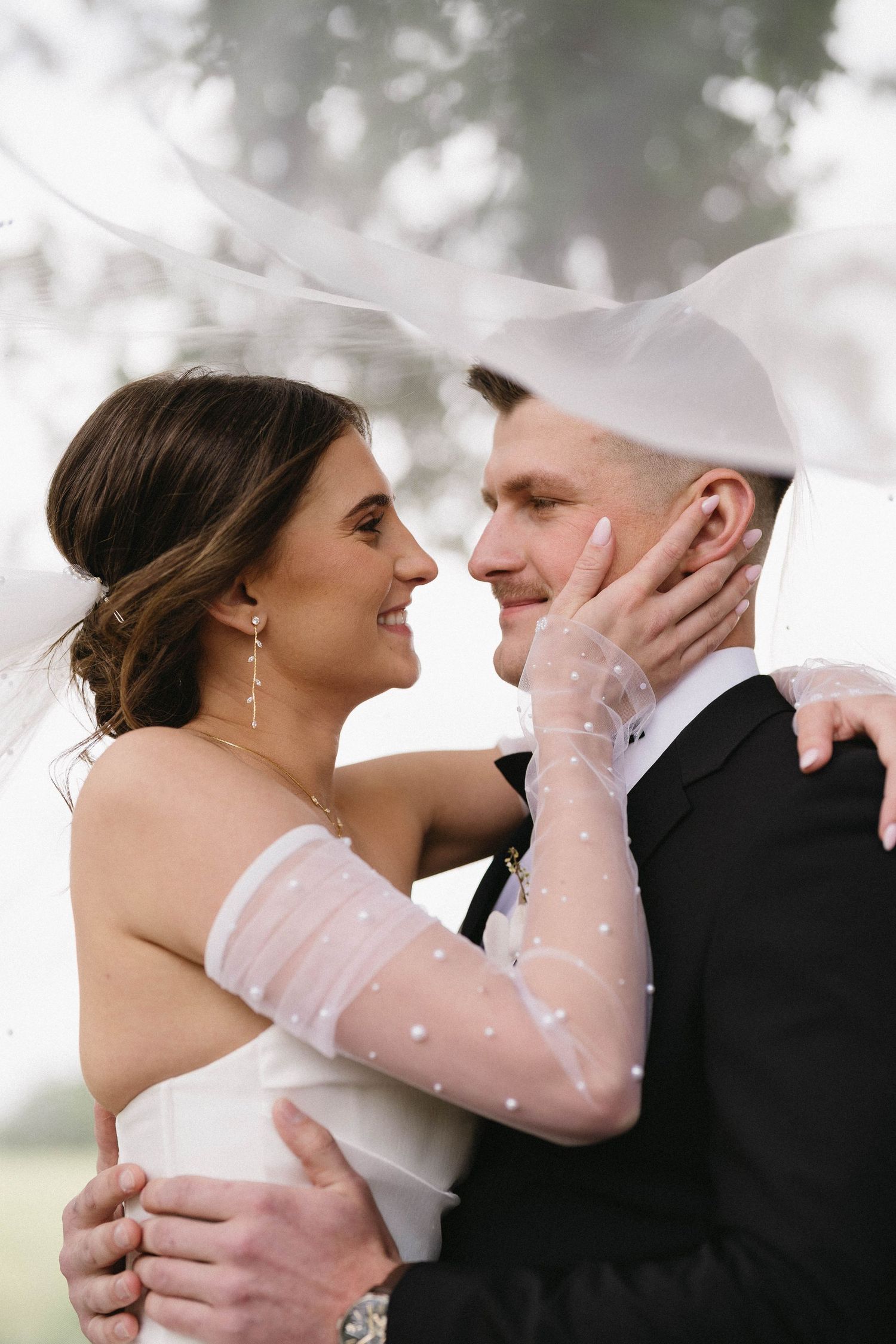 Tender moment between newlyweds as they embrace outdoors with bride wearing sheer dotted sleeves.