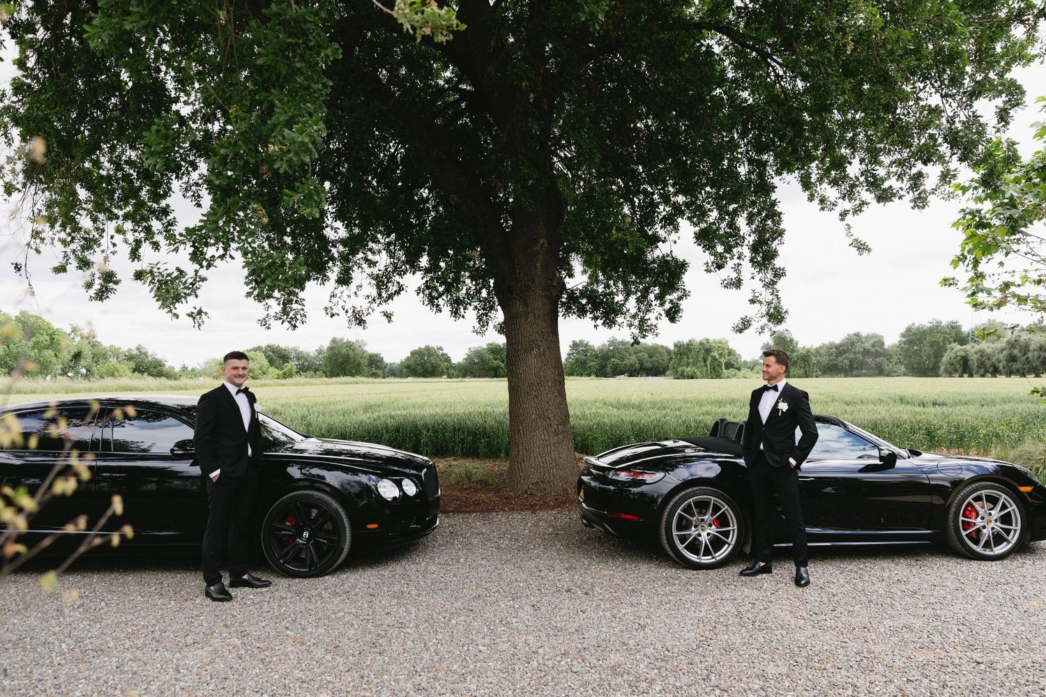 Luxury convertible cars parked under trees at an outdoor wedding venue.