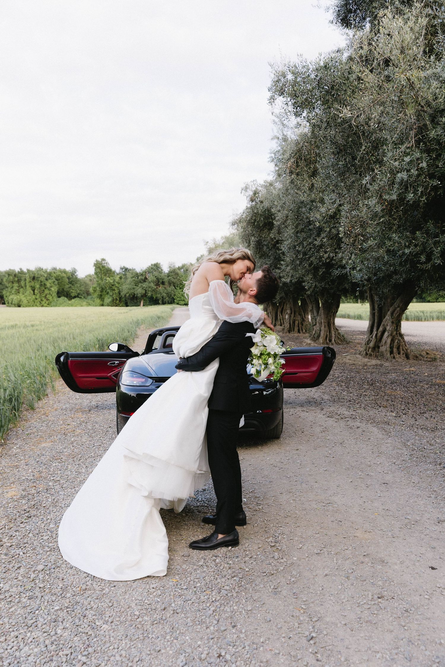 Romantic moment by black convertible car with flowing white wedding dress.