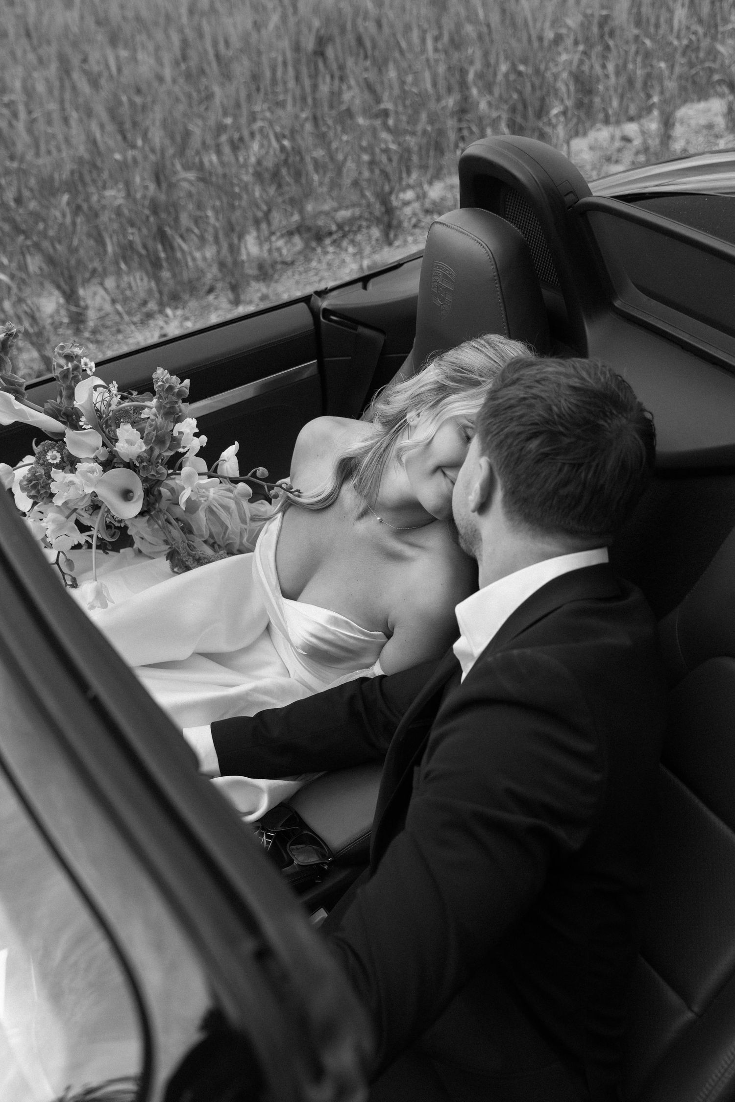 Romantic black and white photo of a couple in formal attire inside a vintage car.
