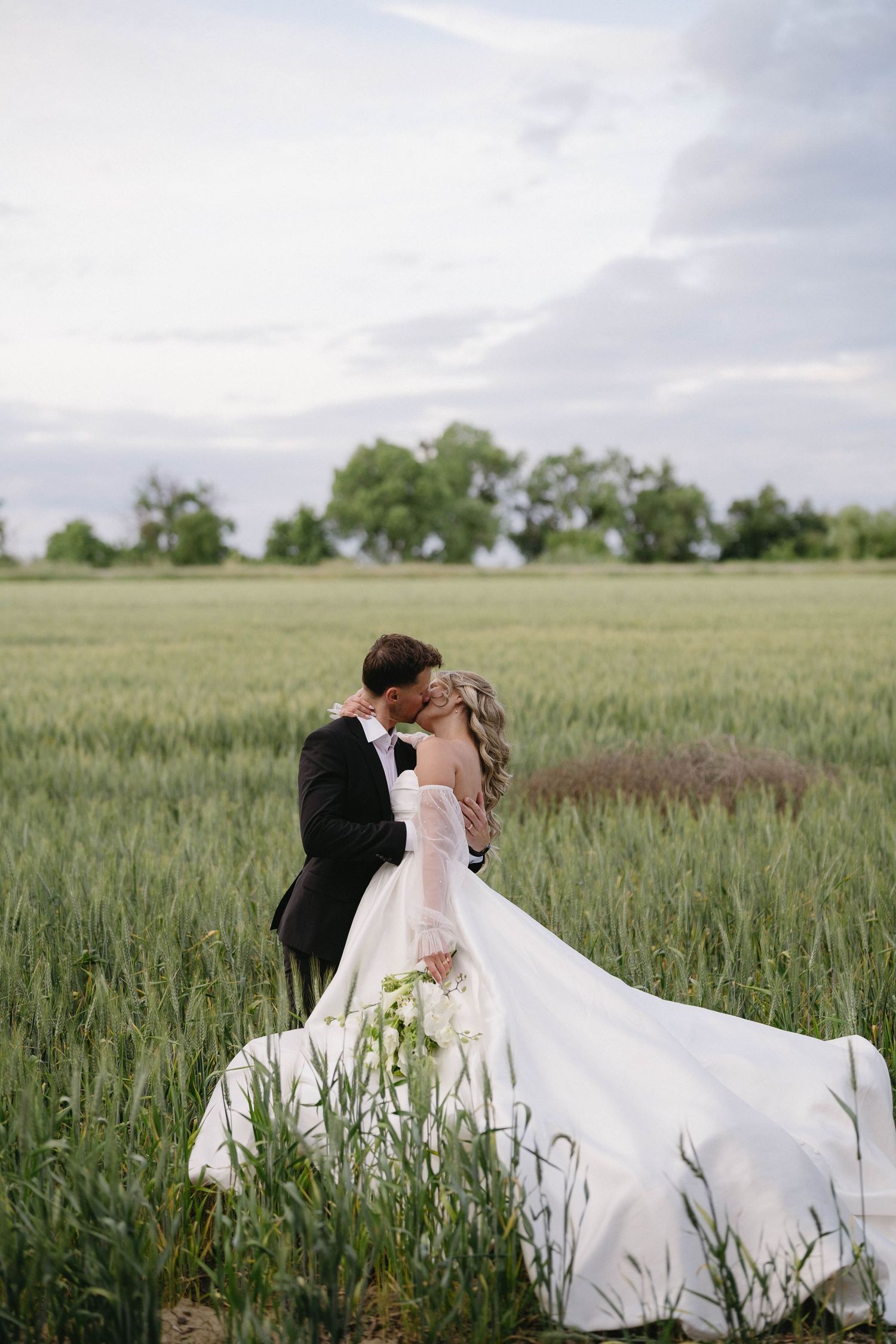 Romantic wedding couple embracing in a vast wheat field with flowing white dress.