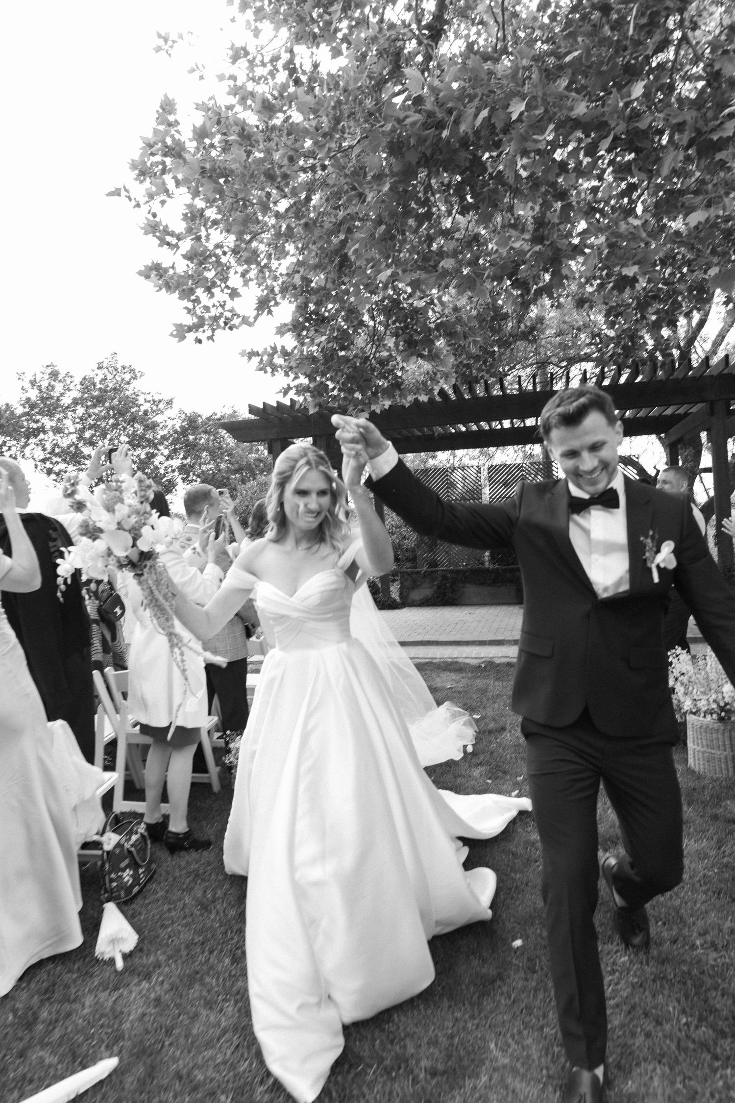 Wedding couple and guests dancing joyfully on a grassy lawn at an outdoor reception.