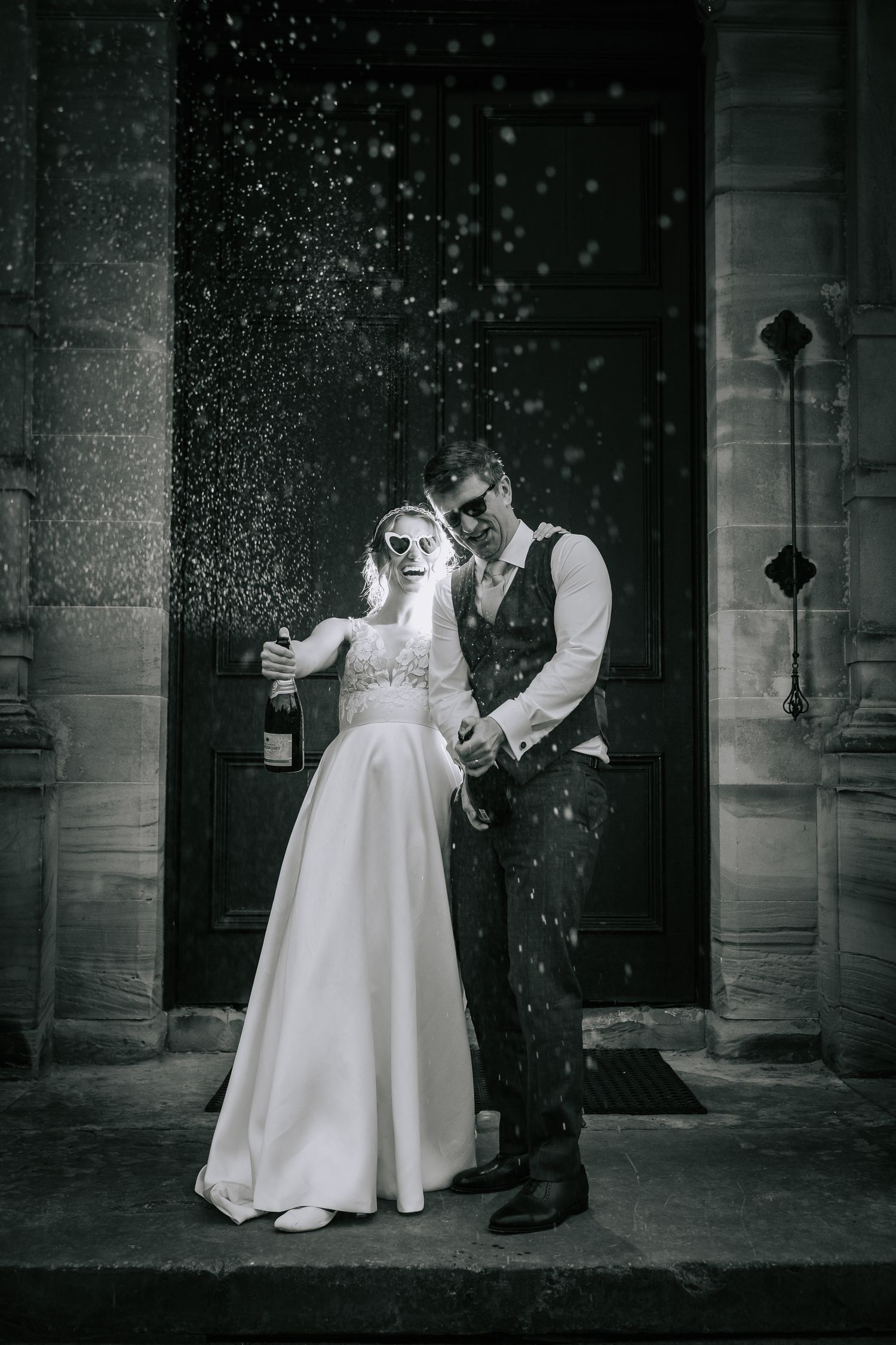 Black and white photo of couple in formal attire standing in doorway while snow falls.