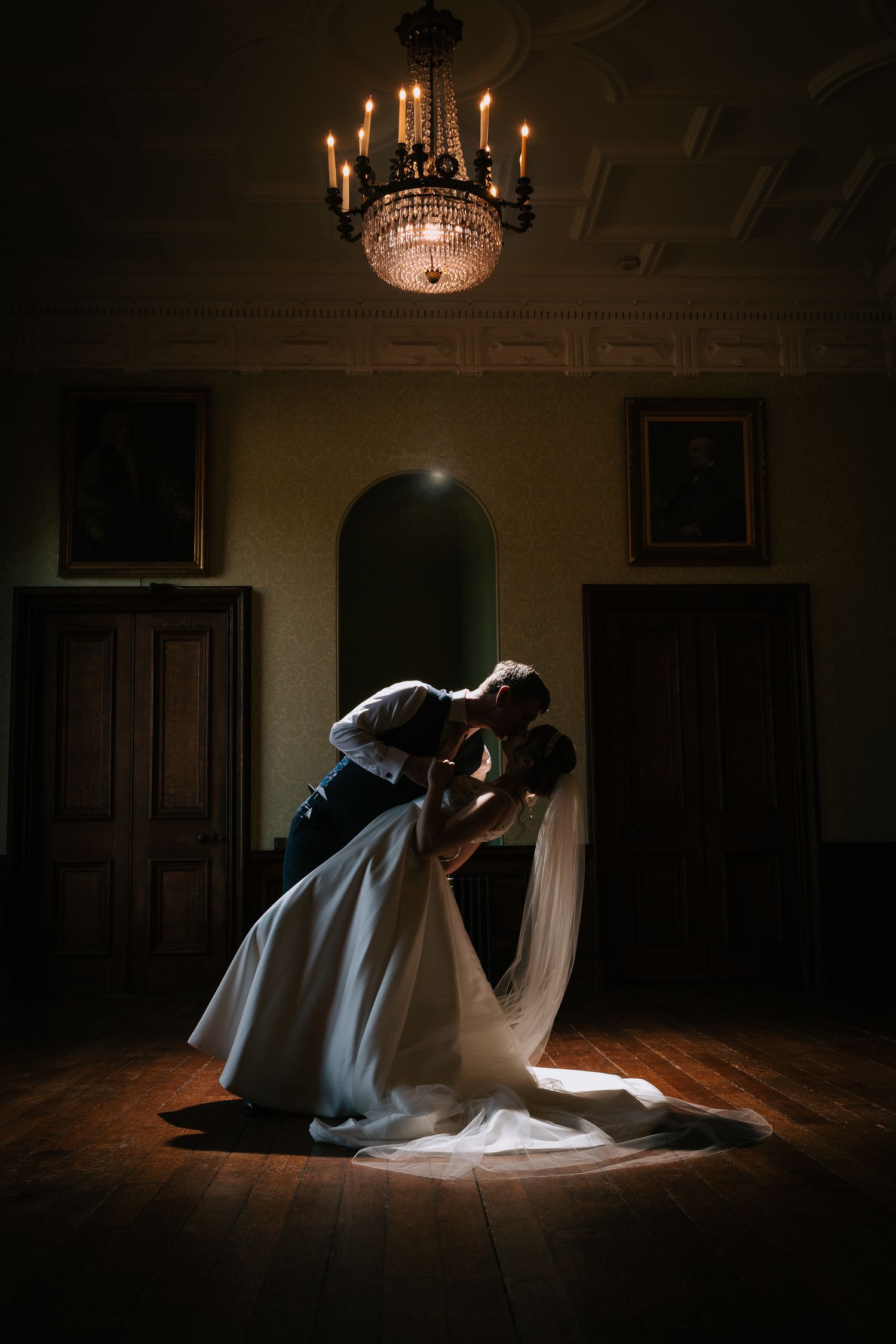 Dramatic dip pose silhouetted under crystal chandelier in elegant ballroom.