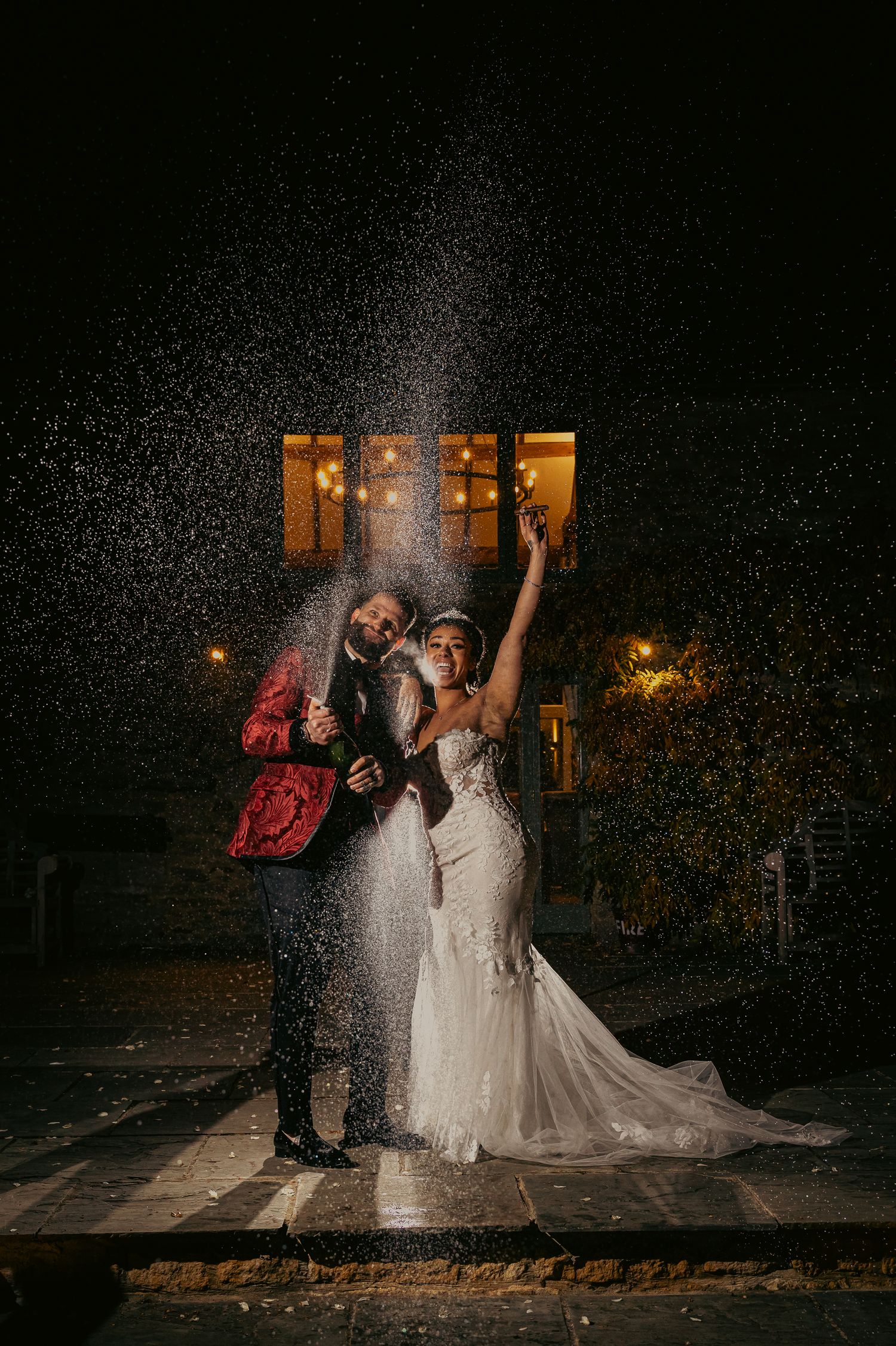 A celebratory wedding photo champagne spray and warm window lights creating a magical nighttime scene.