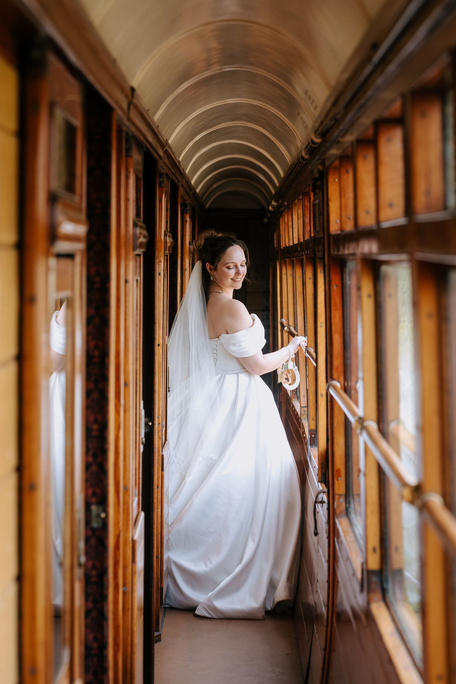 Bride in white gown poses in vintage train corridor with wooden paneling.