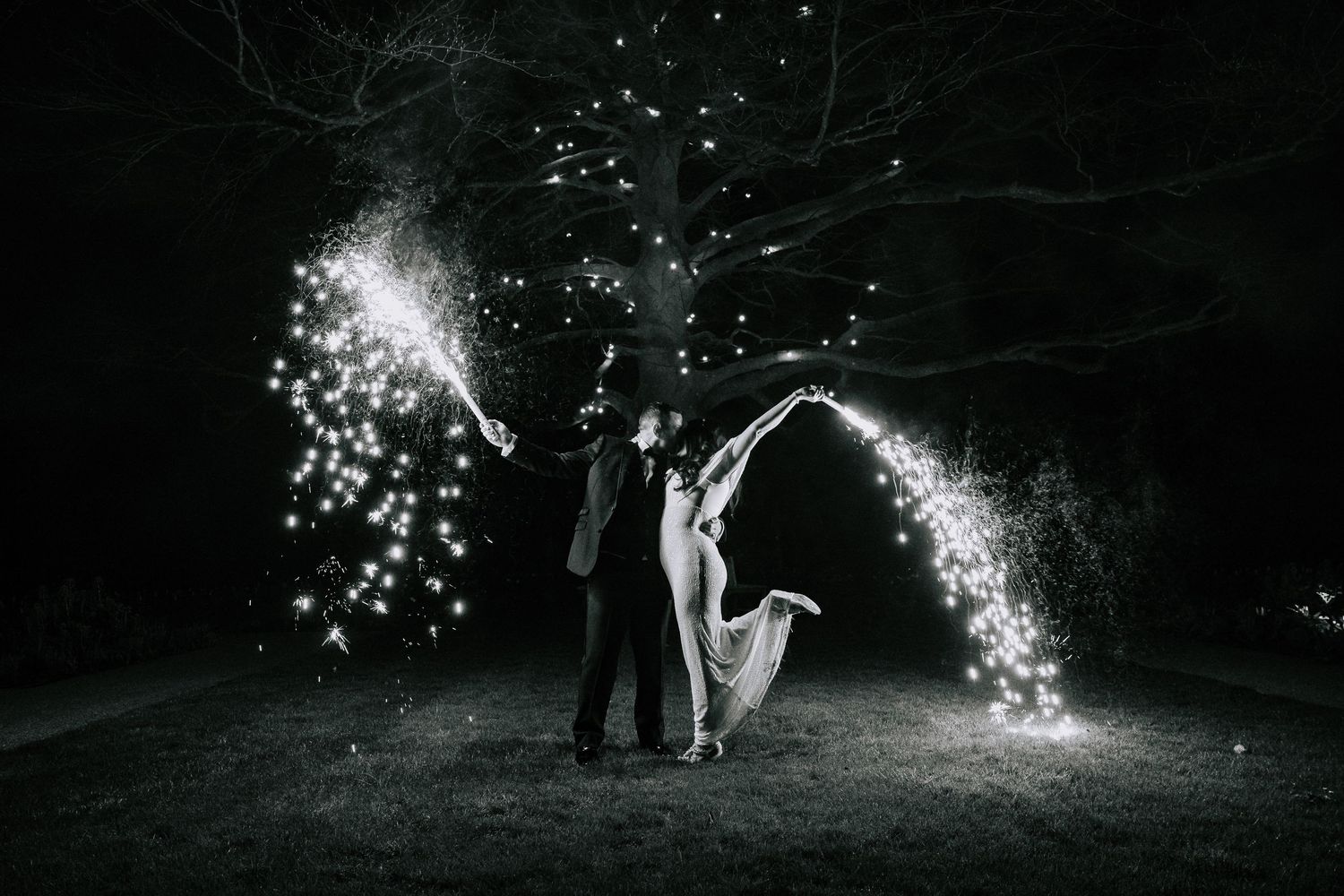 A nighttime wedding photo with sparklers creating magical light arches in the dark.