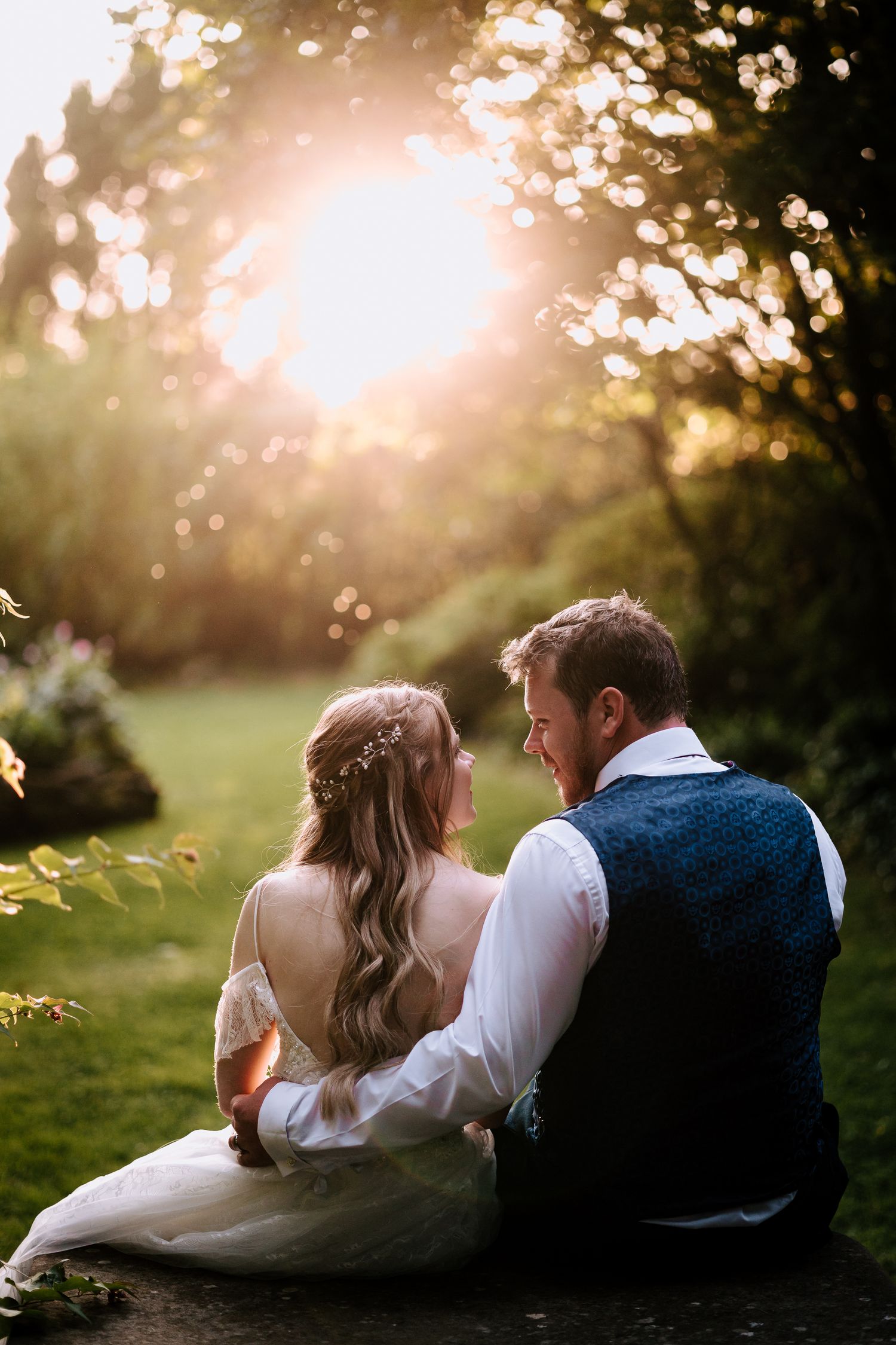 Intimate sunset portrait of couple sitting on grass with golden backlight.