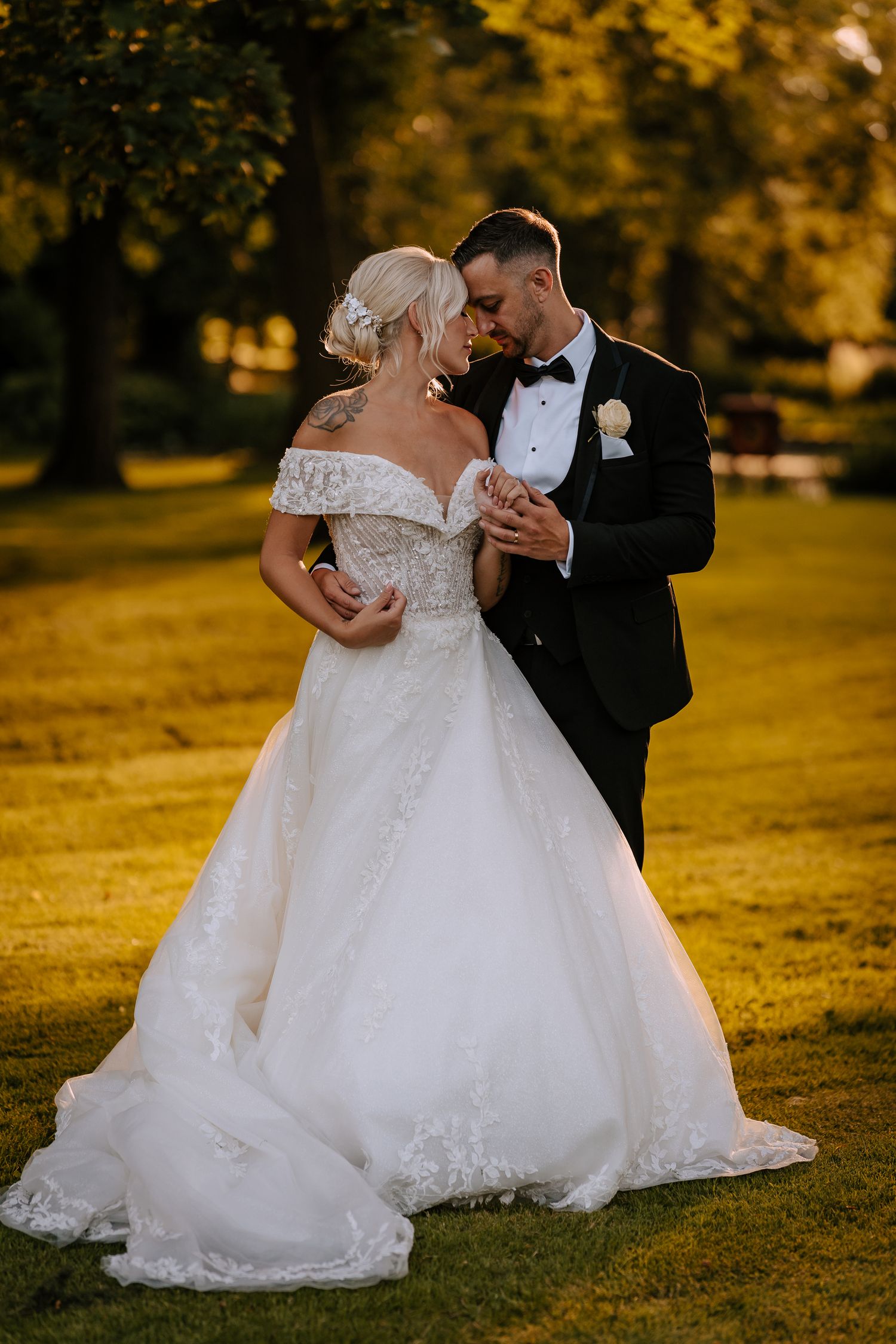 Elegant wedding couple sharing intimate moment on sunlit autumn lawn.