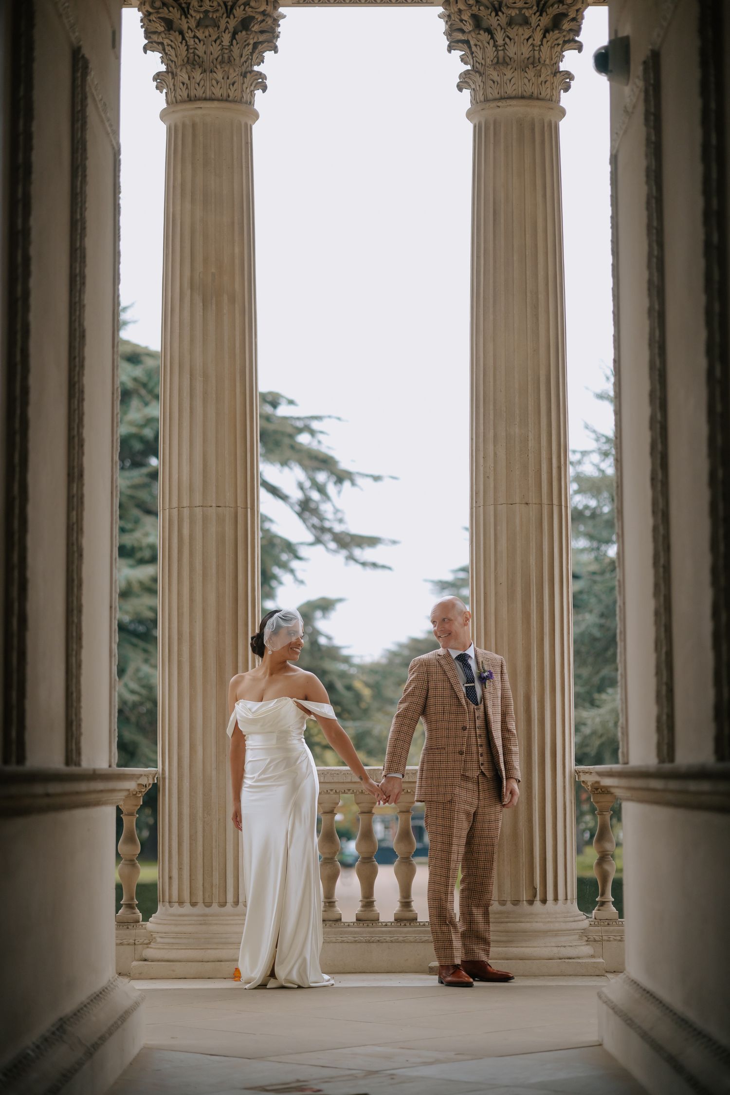 Wedding couple standing between classical stone columns at historic venue.