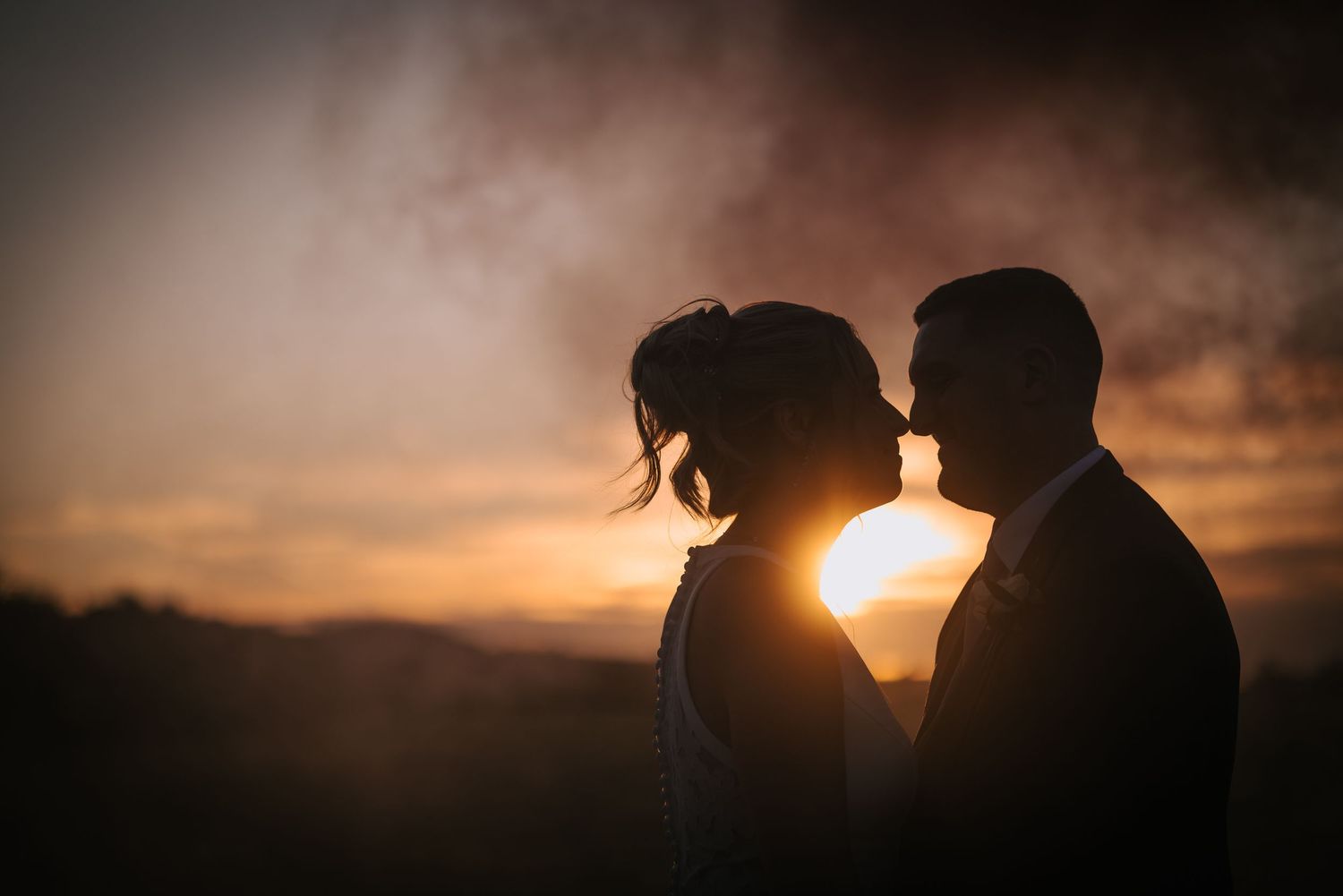 Intimate silhouette portrait of a couple against a warm sunset backdrop in nature.