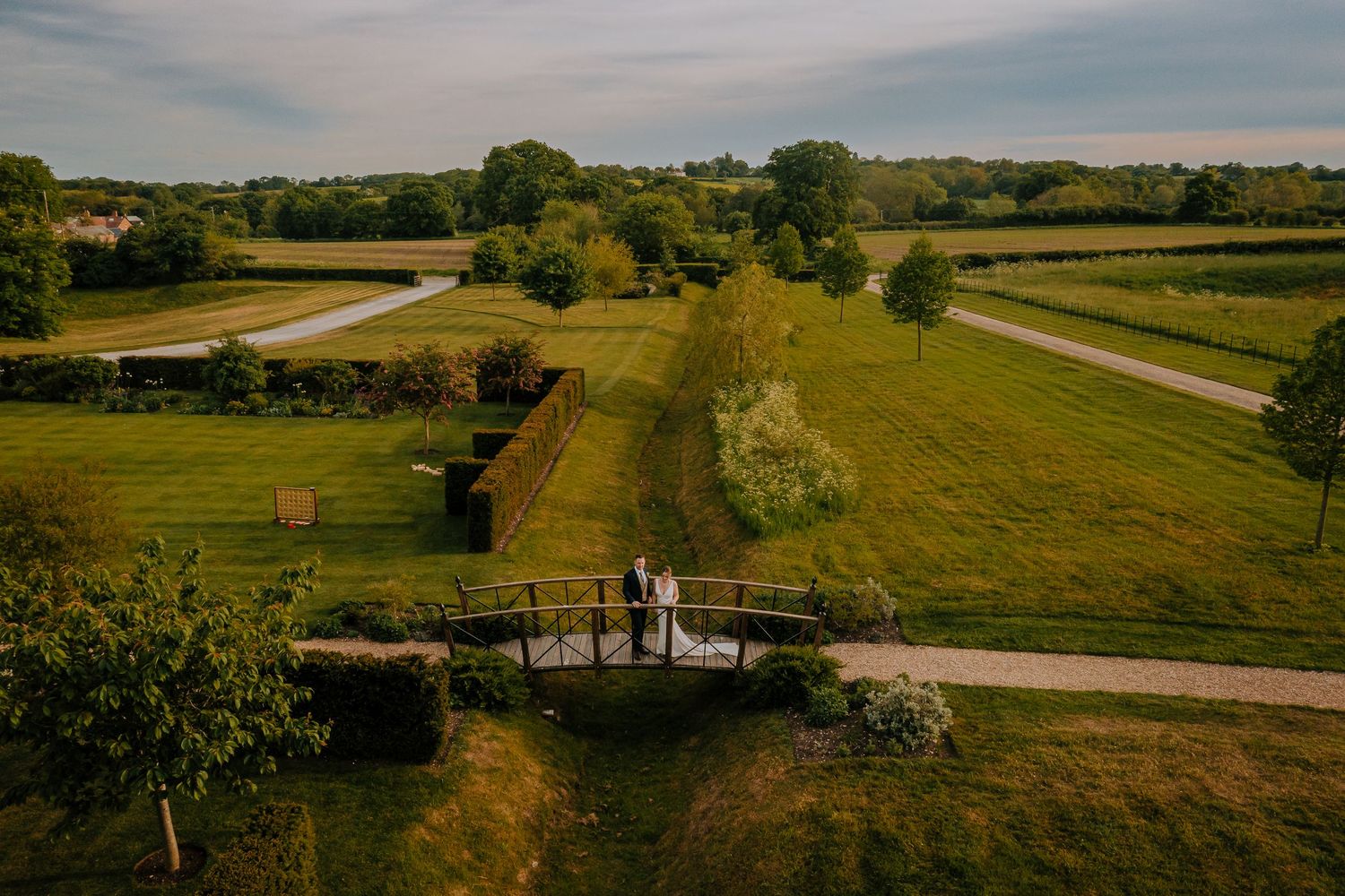 An aerial view of a couple crossing a bridge in a vast countryside landscape.