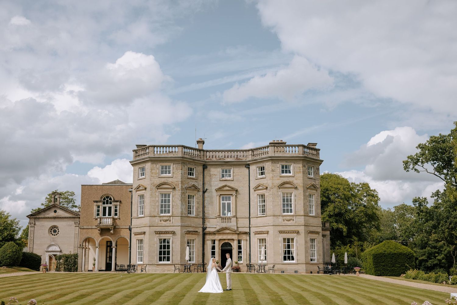 Grand estate wedding venue with classical architecture and manicured lawns on sunny day.