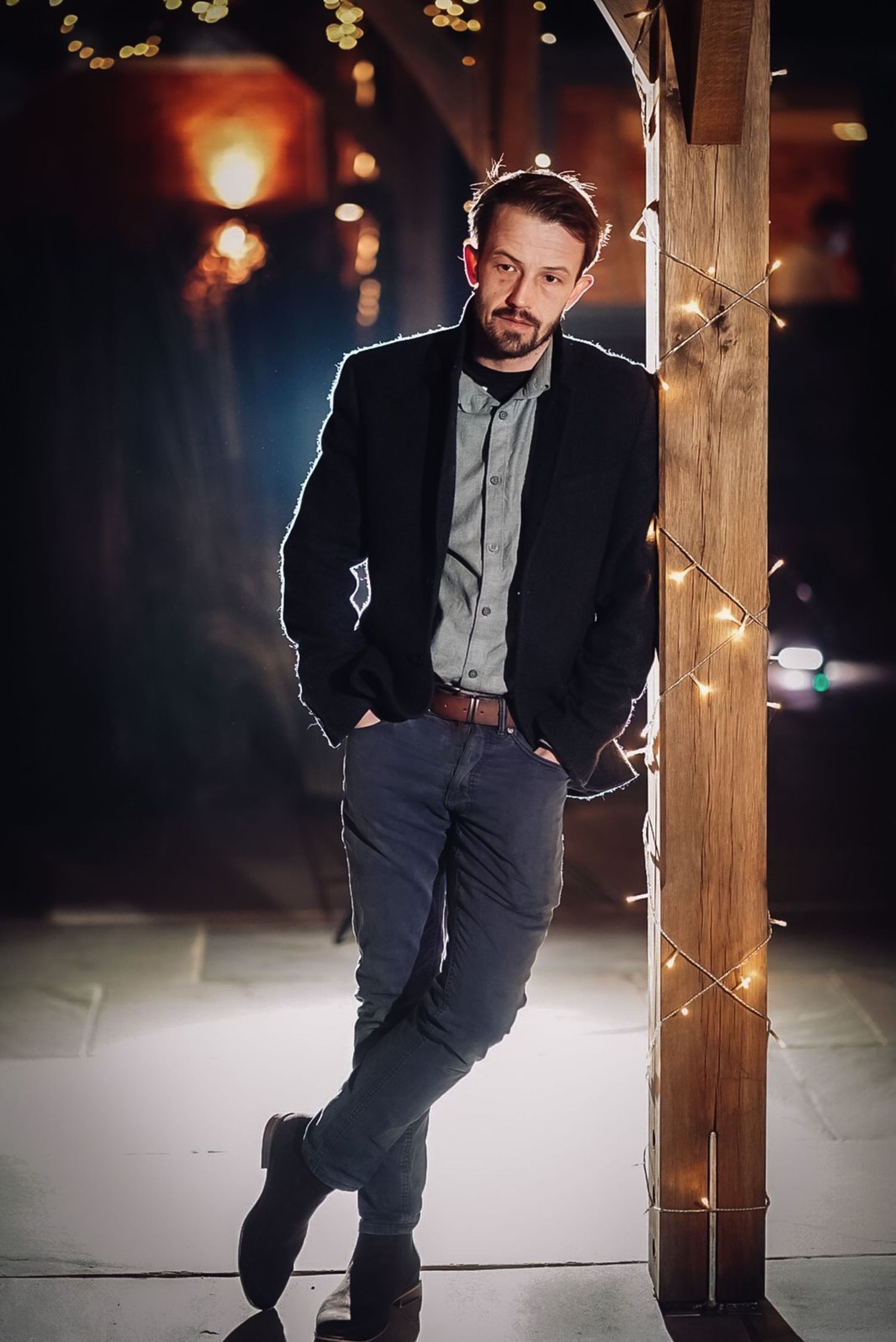 Evening portrait with string lights and wooden post creating dramatic ambiance.