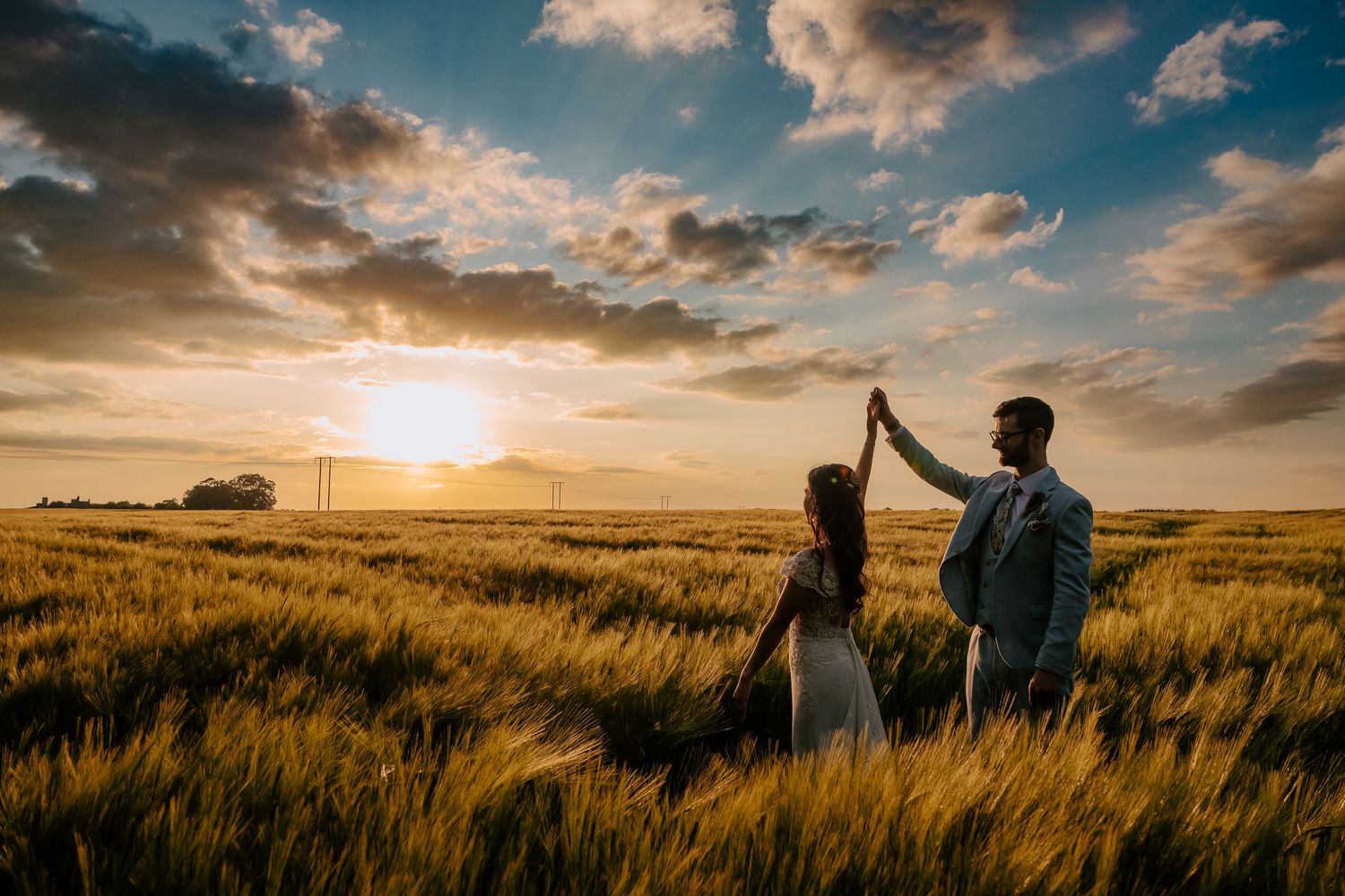 Romantic silhouettes celebrating at sunset in a golden wheat field with dramatic clouds in the sky.