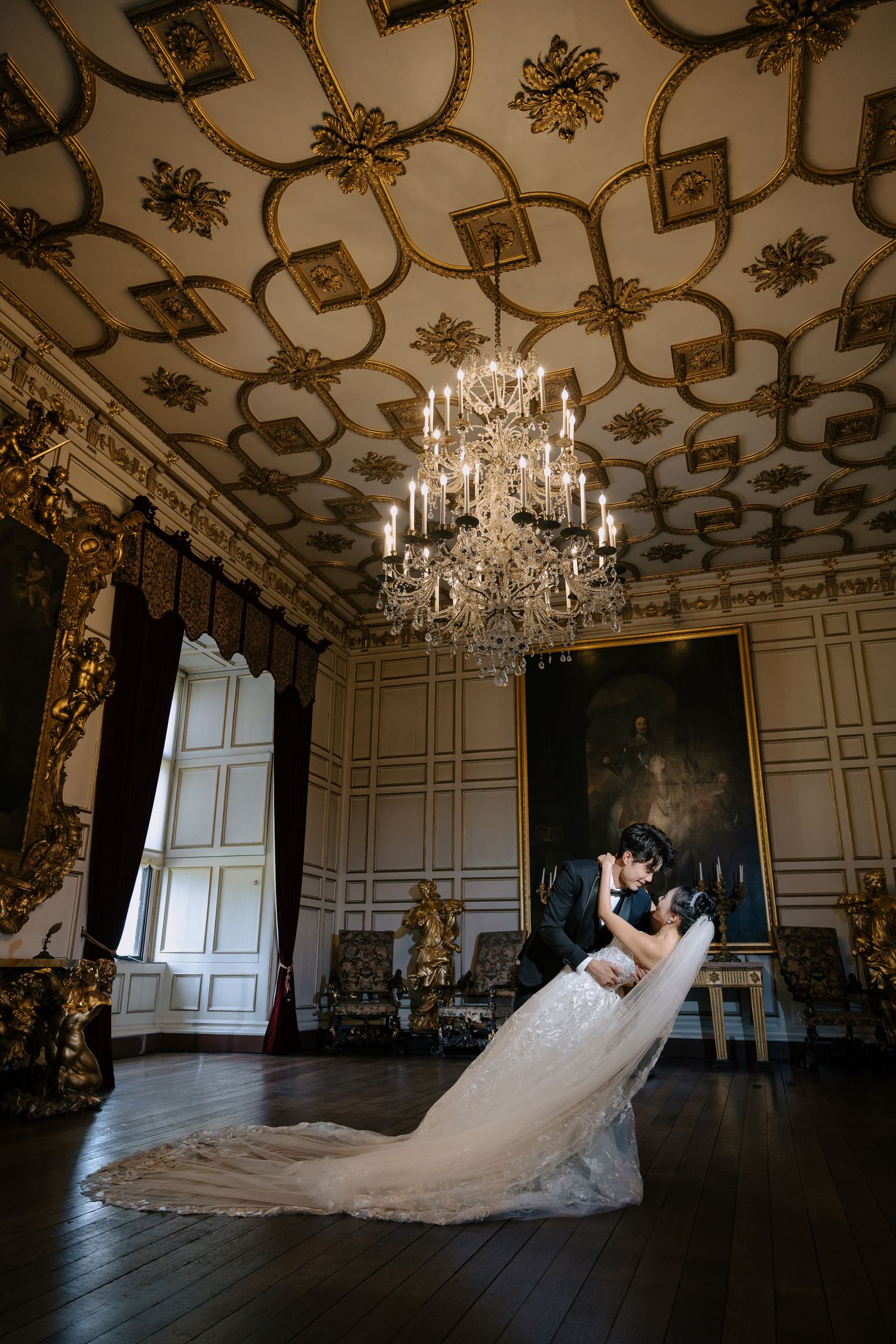 Elegant ballroom wedding photo with ornate ceiling, chandelier and flowing white gown.