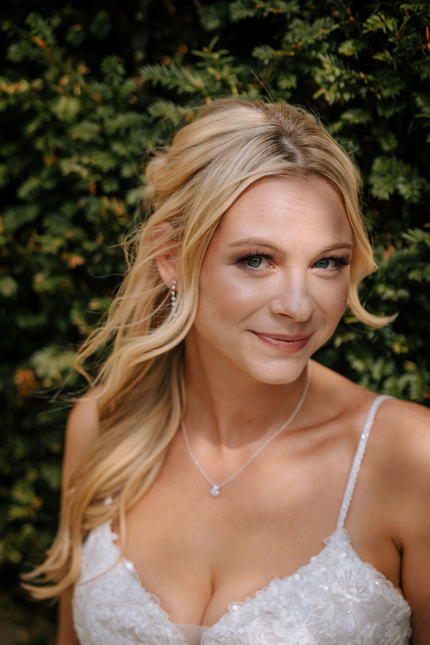 Close-up portrait of bride in lace dress against natural foliage background.