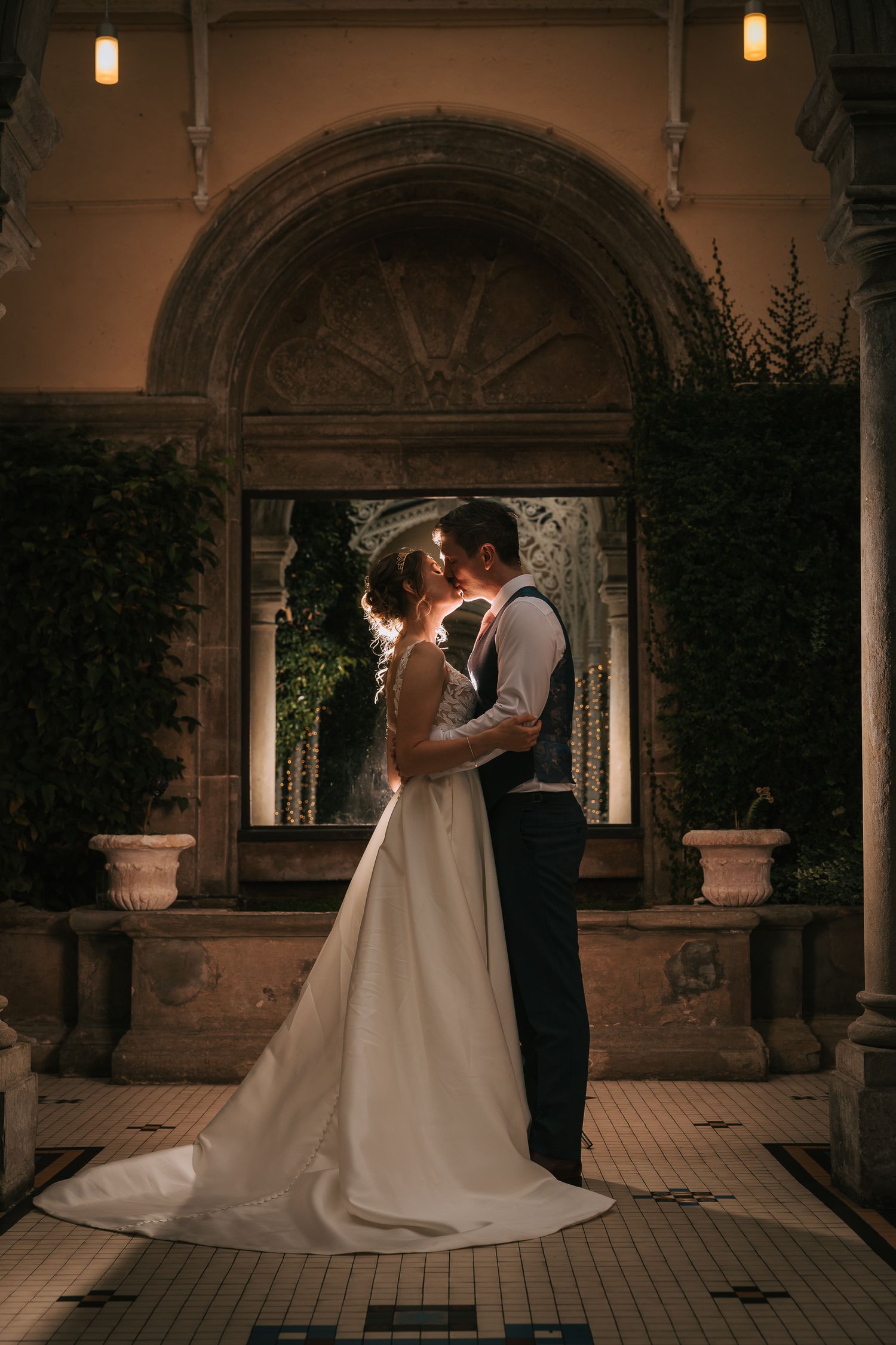 Wedding couple embraces under arched doorway at dusk with romantic lighting.