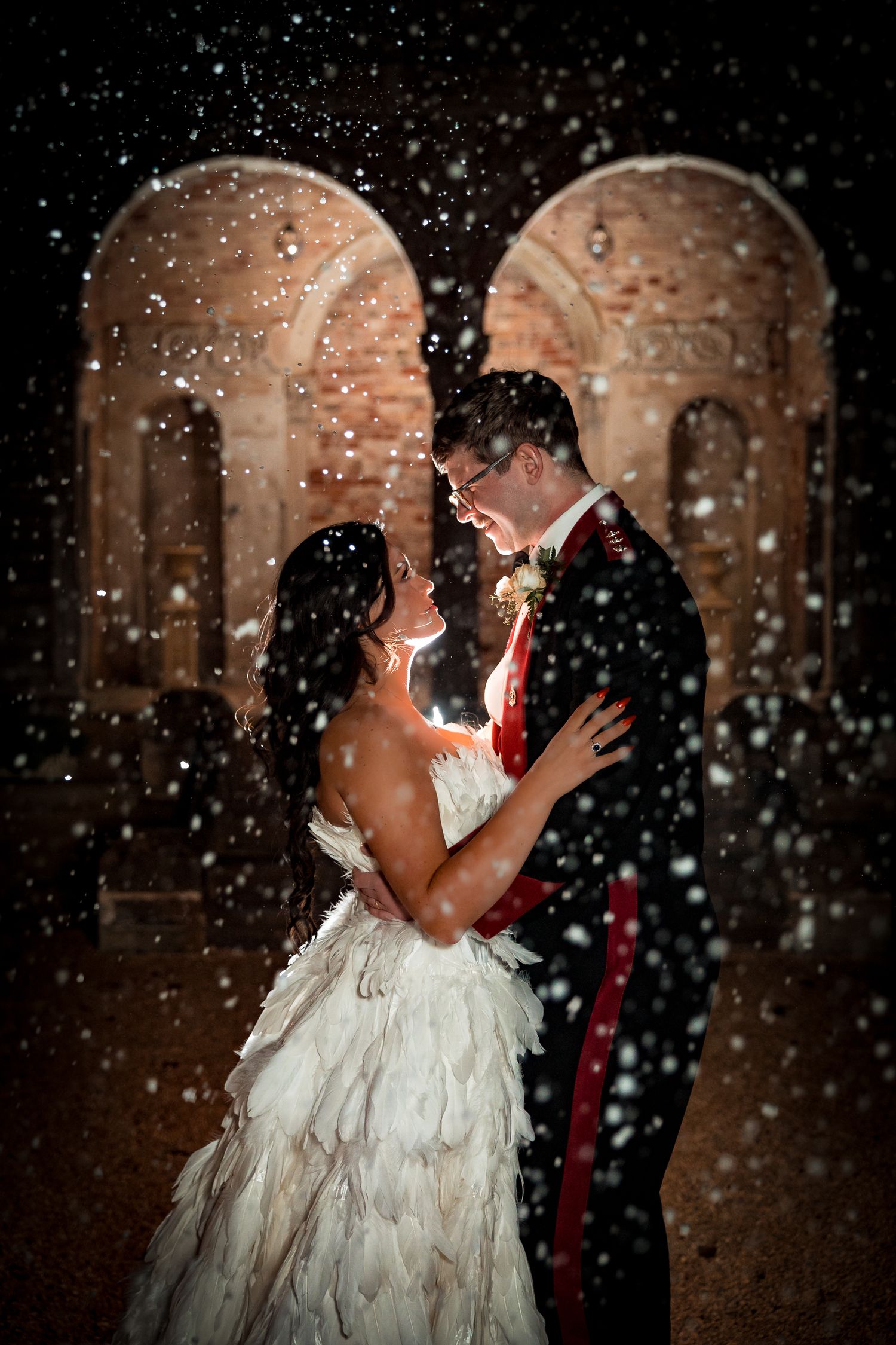 A romantic winter wedding portrait with falling snow and arched doorways creating a magical atmosphere.