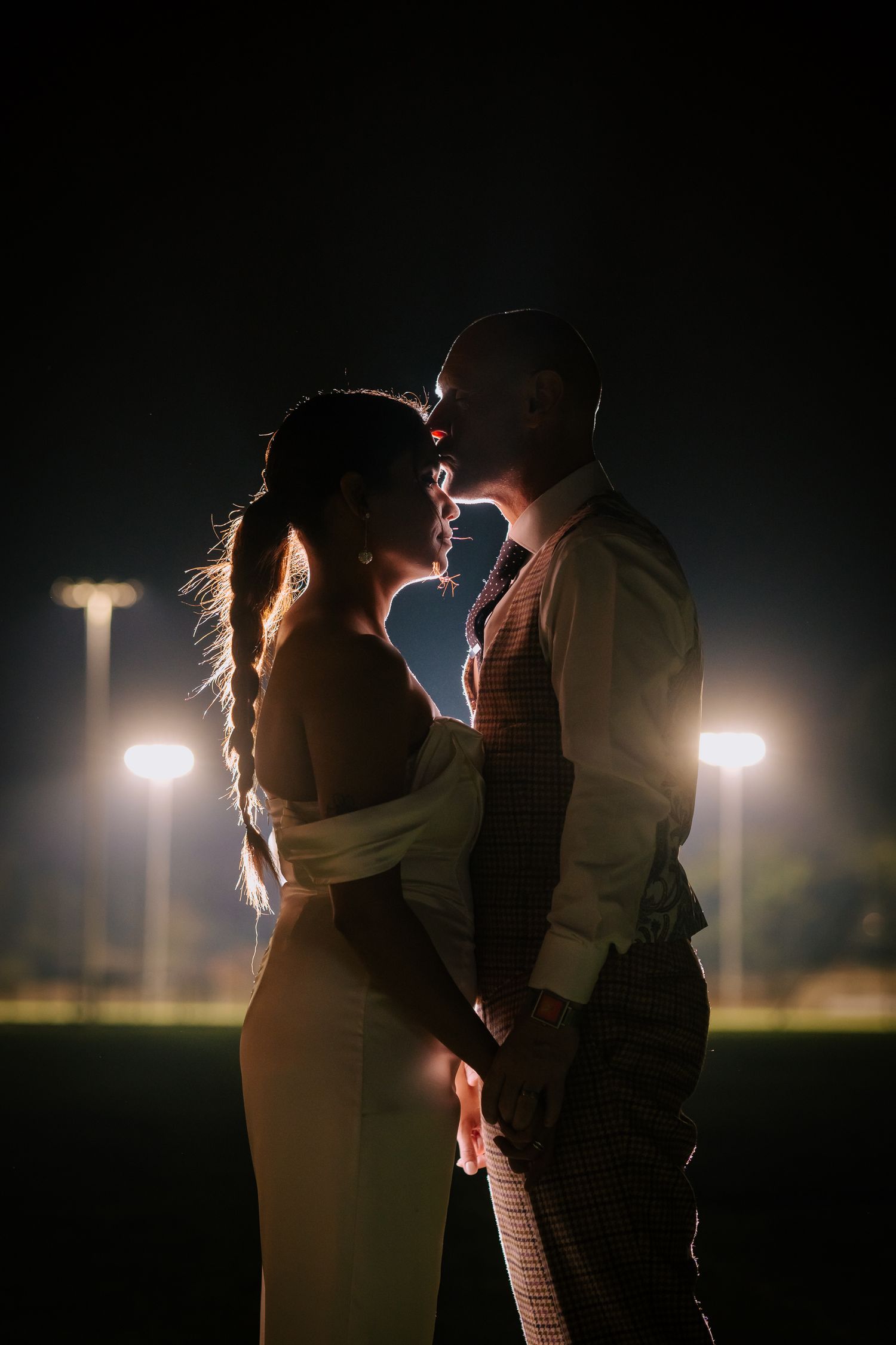 Romantic nighttime portrait of couple illuminated by stadium lights.