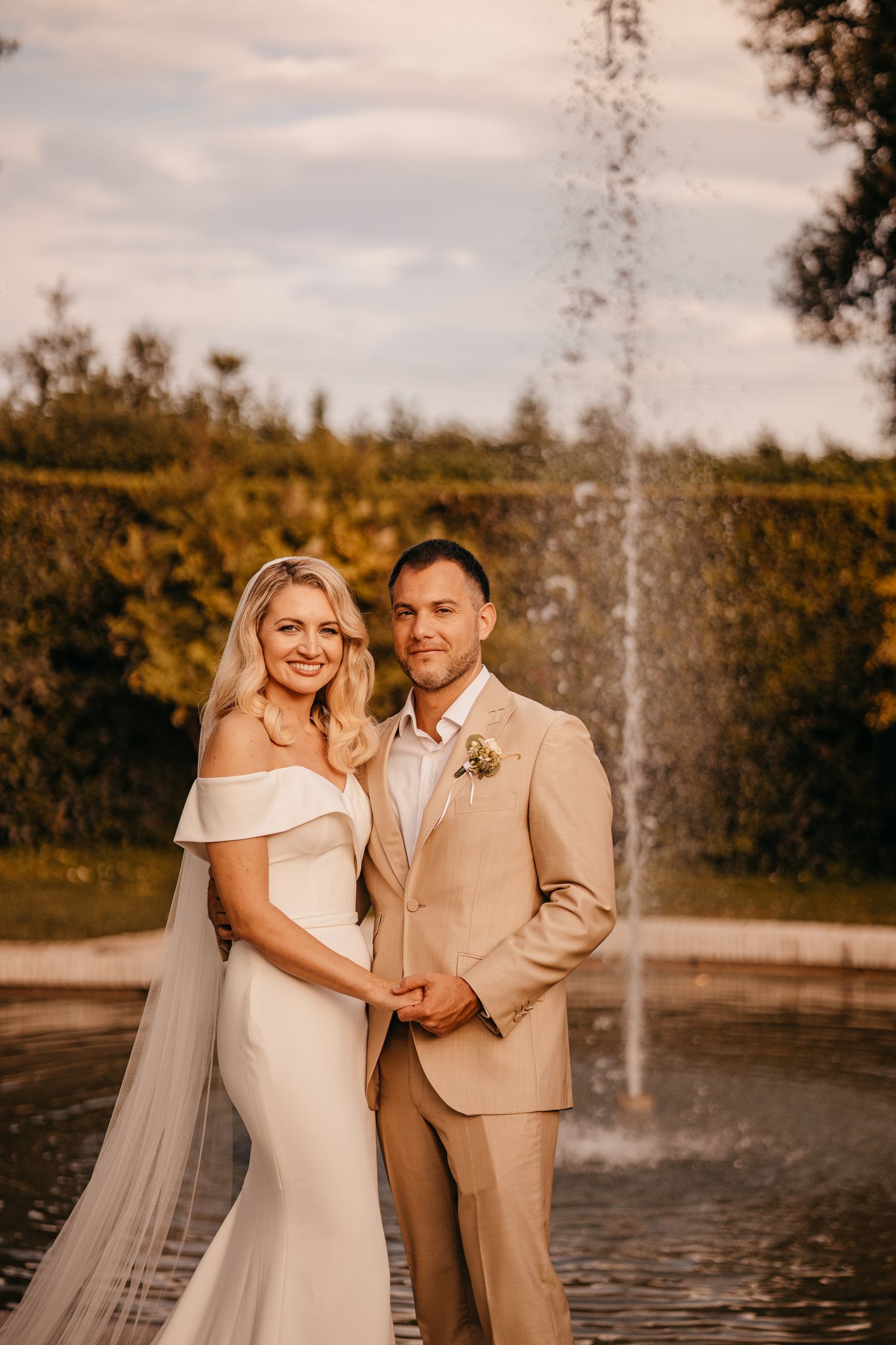 Wedding portrait by a fountain with couple in ivory and tan attire during golden hour.