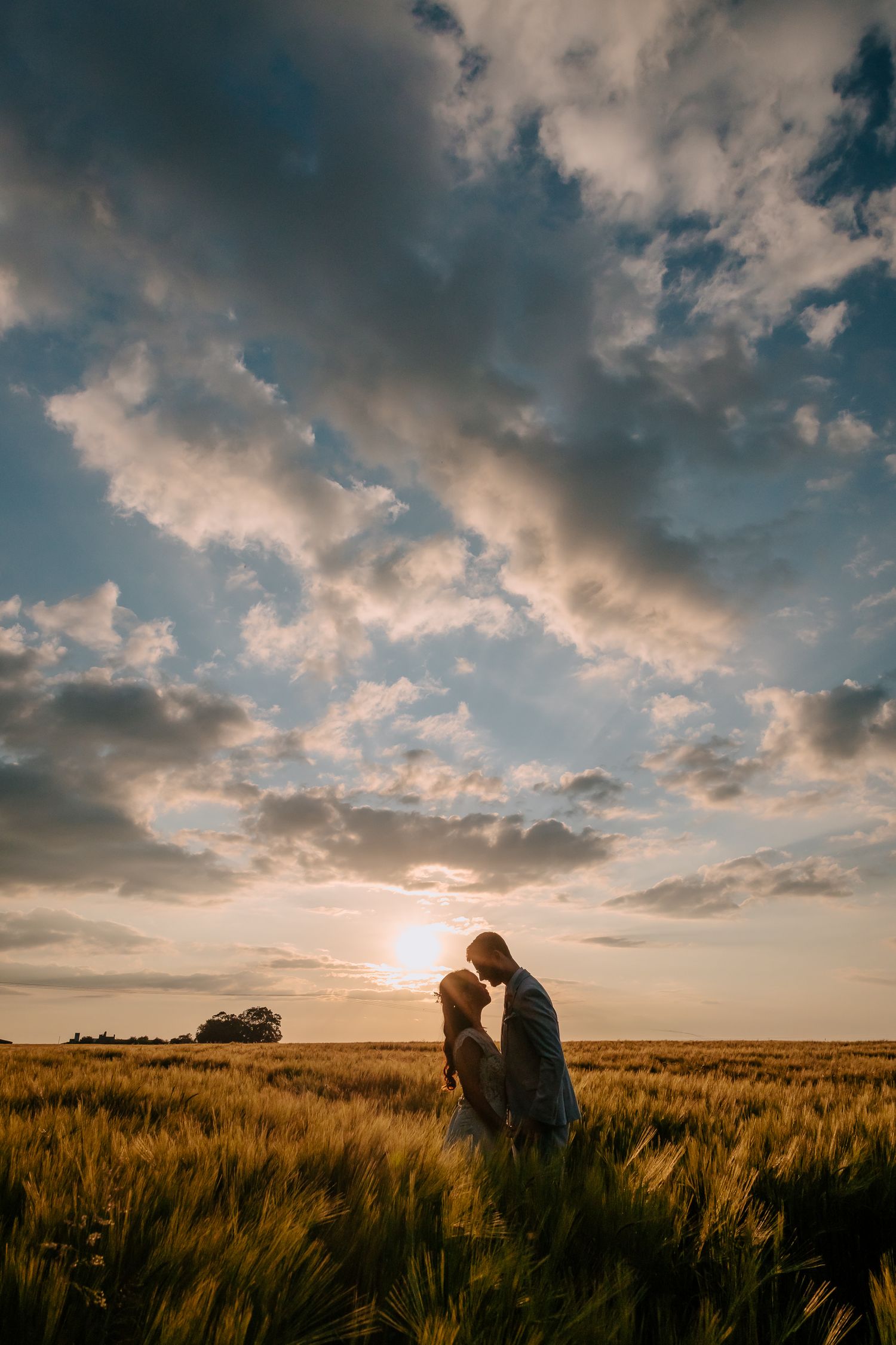 Wedding couple silhouetted against golden sunset sky in wheat field at magic hour.