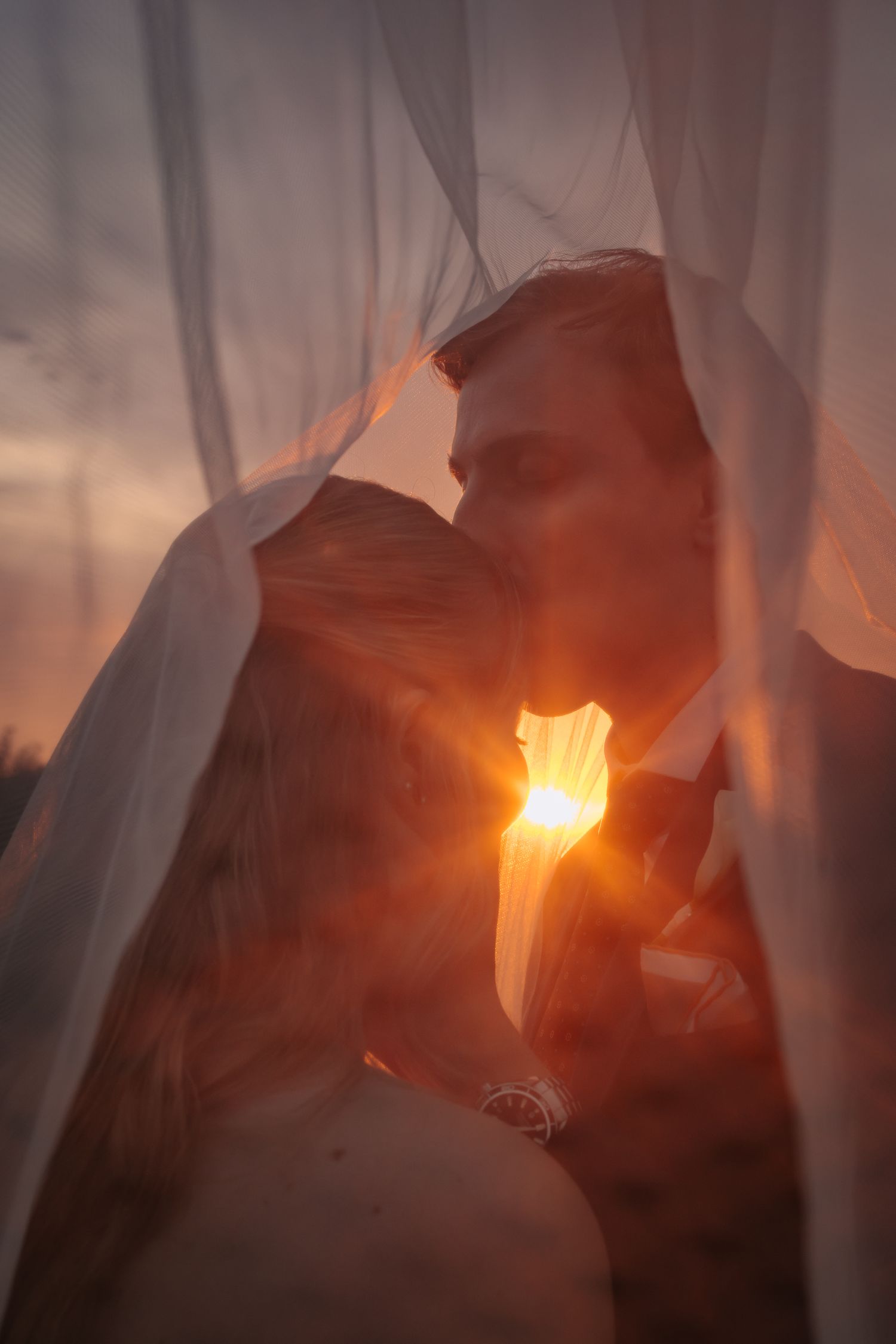 Ethereal wedding photo through flowing veil with glowing sunset light creating a romantic atmosphere.