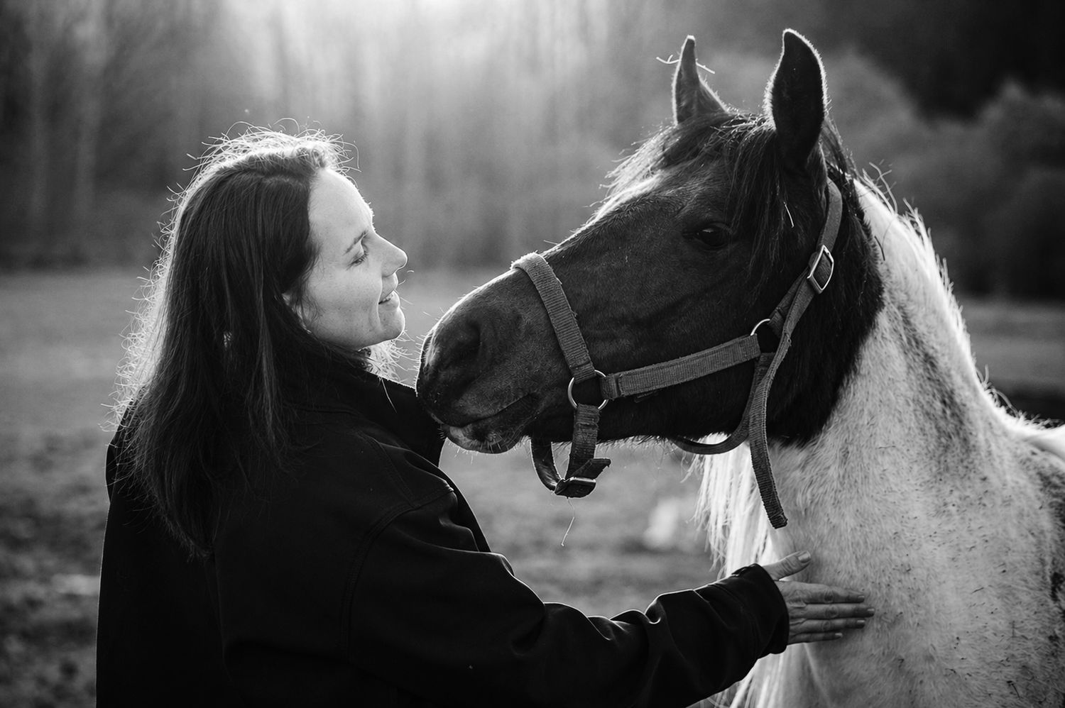 Black and white photo of a woman tenderly bonding with a horse outdoors in soft natural light.