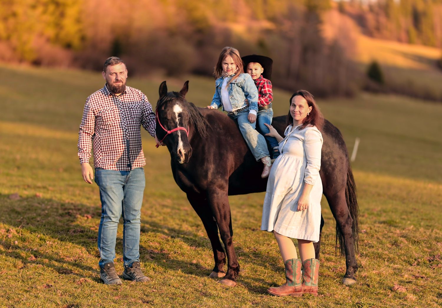 Family with two children riding a black horse in a sunny autumn field.