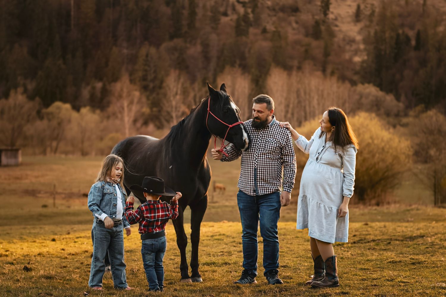 Family with two children and a black horse in an autumn field with trees in the background.