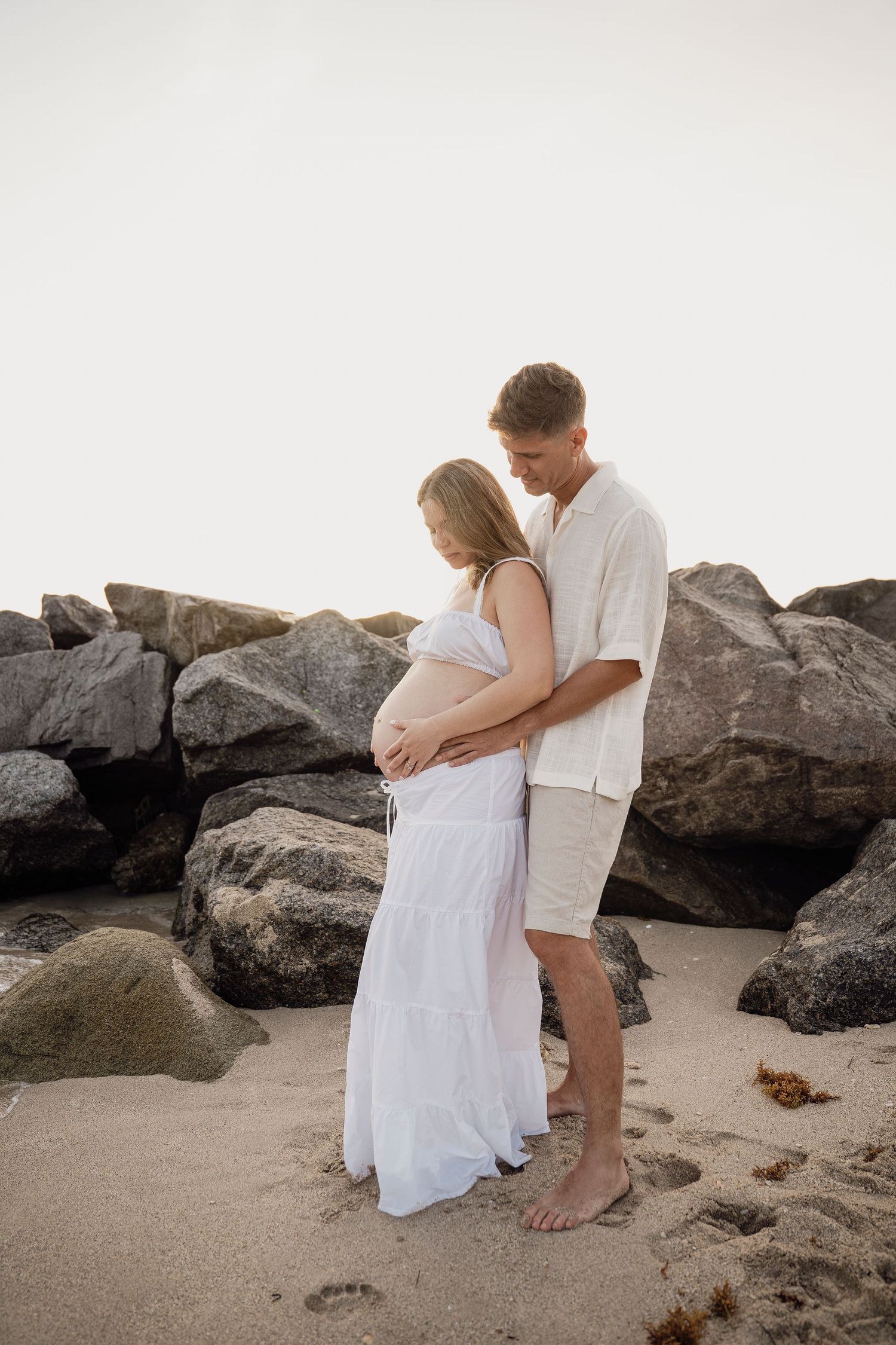 Couple in white outfits sharing intimate moments among coastal rocks.