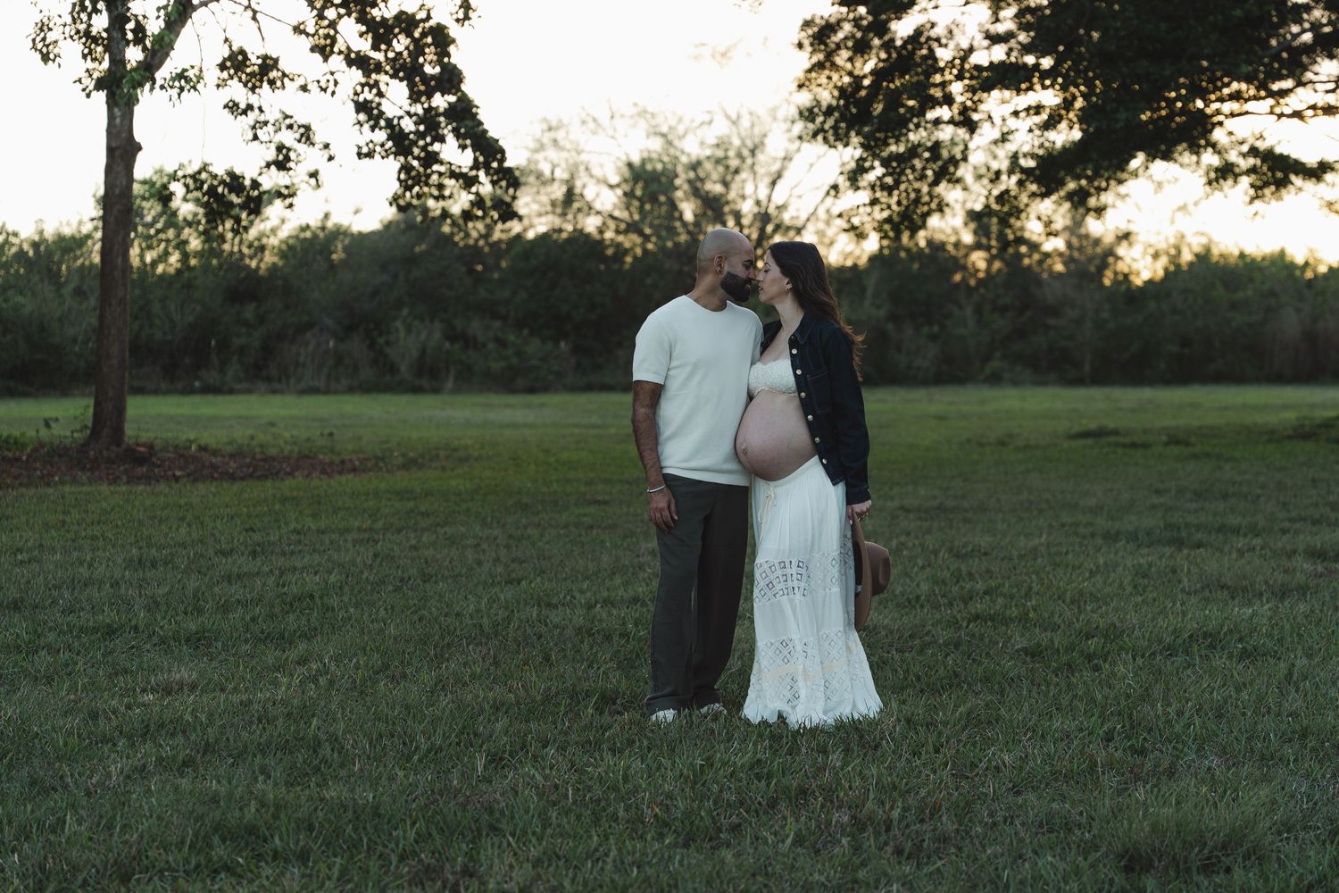 A couple walks hand in hand through a grassy field at sunset creating a romantic silhouette against the sky.