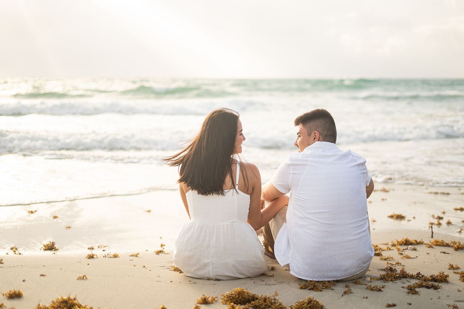 A couple sits together on a sandy beach watching the ocean waves.