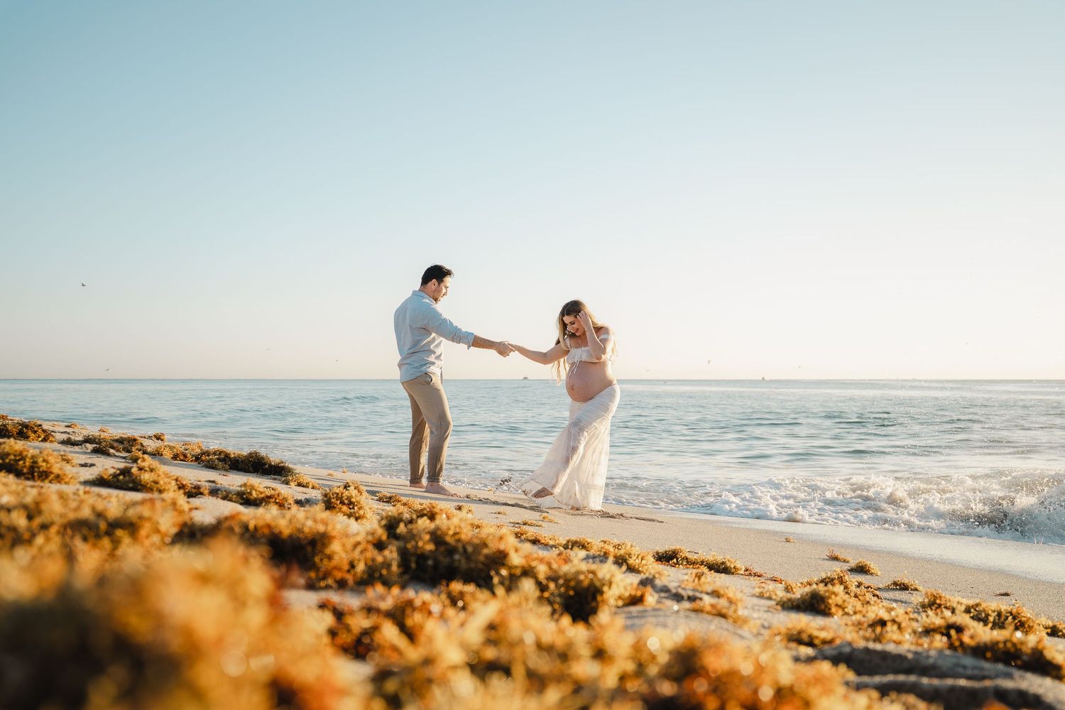 A couple dances together on a golden sandy beach at sunset with ocean waves in the background.